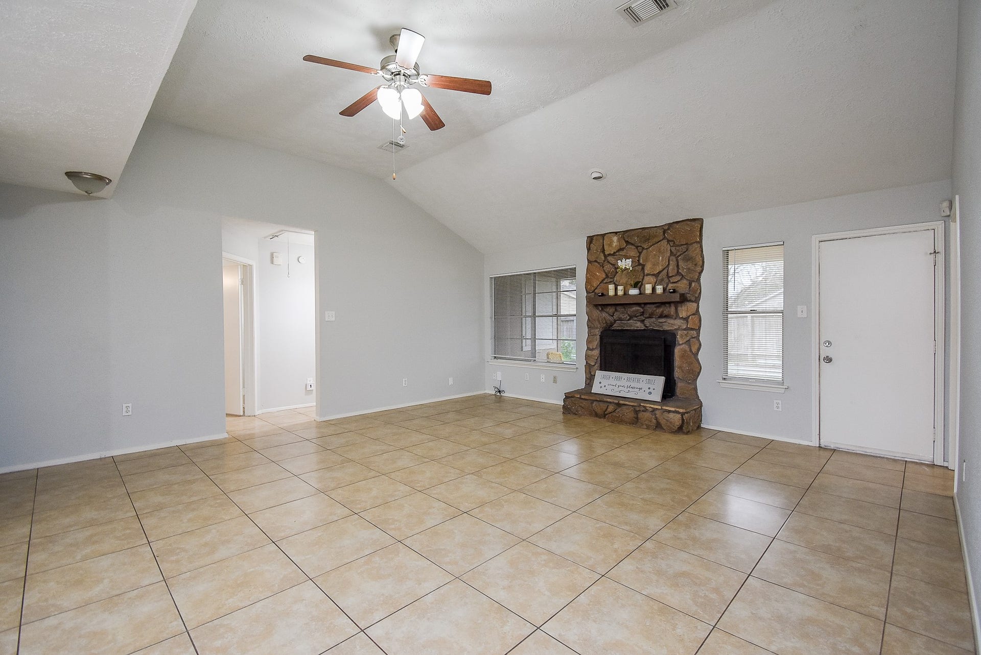 16806 Red Gully Drive, Sugar Land, TX 77498 Spacious living room with vaulted ceiling, tile flooring, and a stone fireplace. Plenty of natural light from large windows, and there's a ceiling fan for comfort.