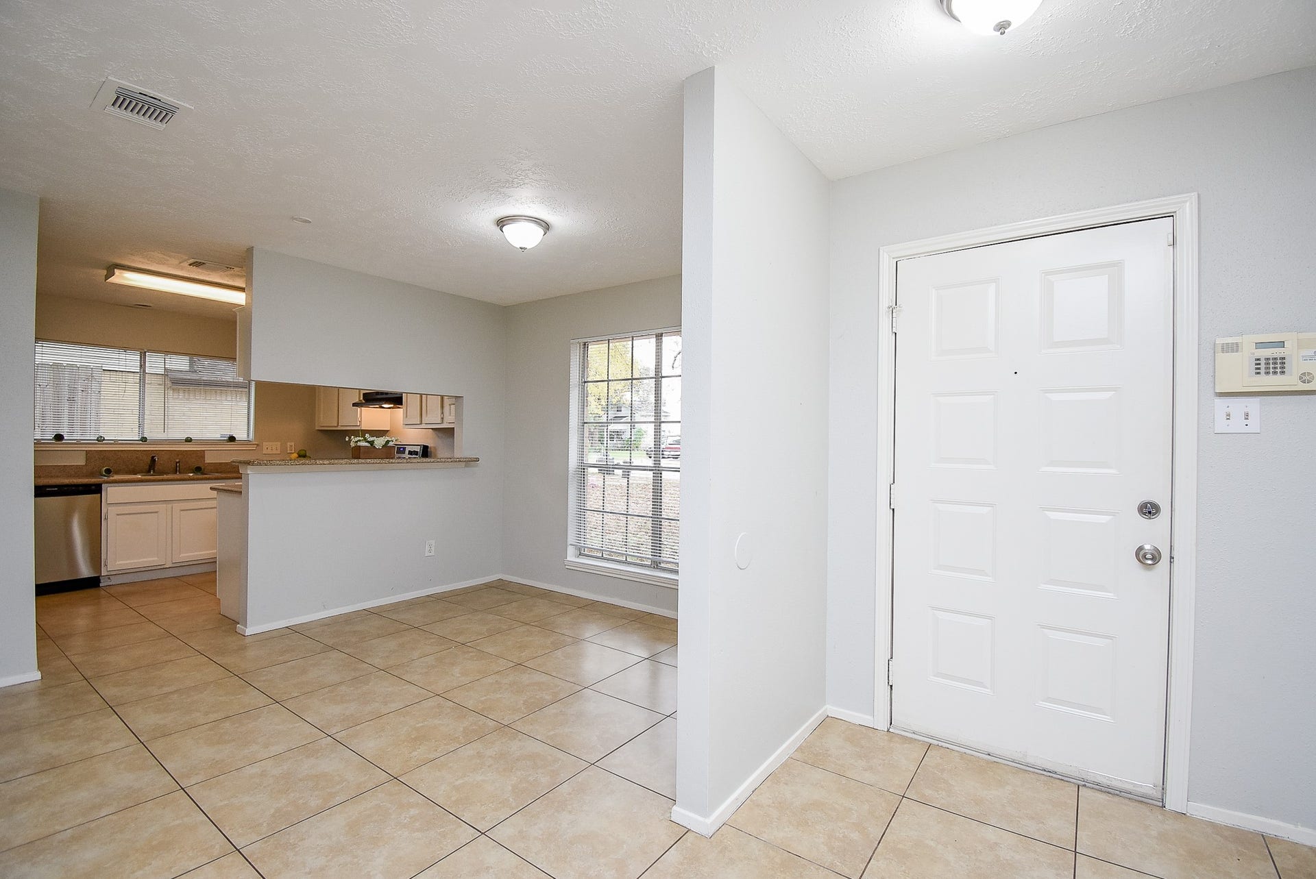 16806 Red Gully Drive, Sugar Land, TX 77498 This photo shows a modern entryway with light tile flooring and neutral walls. It opens into a bright, open-concept kitchen and dining area with ample natural light from large windows. The kitchen features sleek countertops and stainless steel appliances.