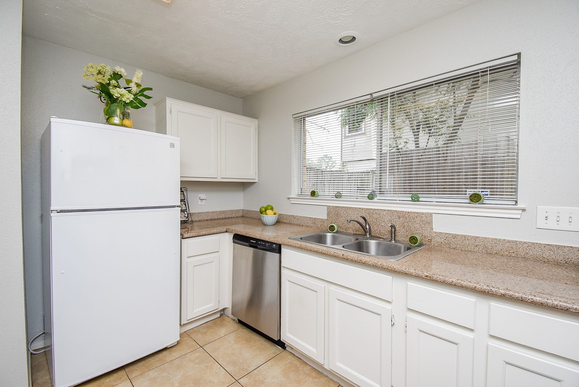16806 Red Gully Drive, Sugar Land, TX 77498 Bright kitchen with white cabinets, granite countertops, and a double sink. Features a large window for natural light, a white refrigerator, and a stainless steel dishwasher. The space feels clean and modern.