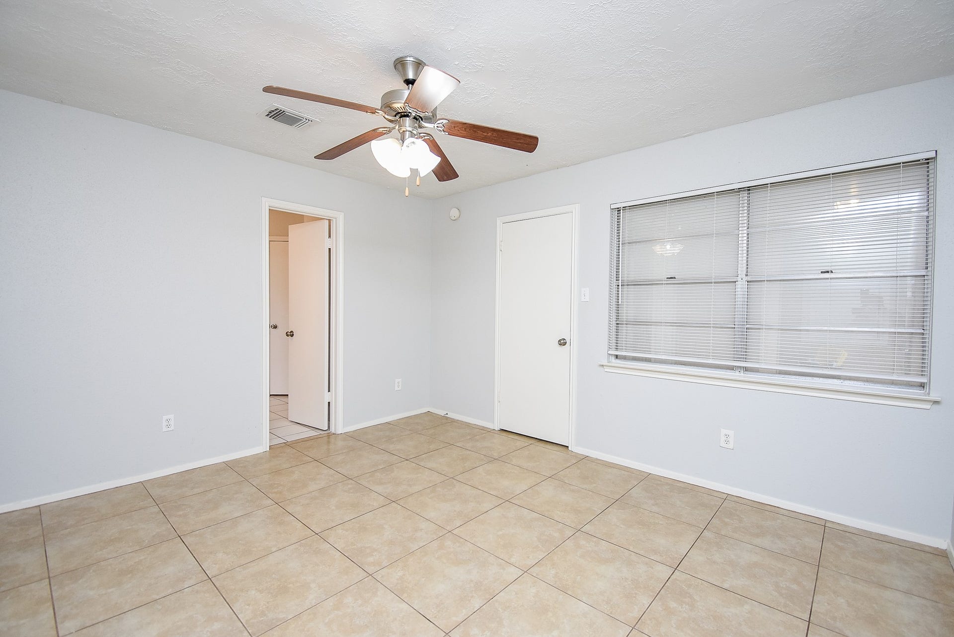 16806 Red Gully Drive, Sugar Land, TX 77498 This bright room features neutral tile flooring, a ceiling fan for added comfort, and large window blinds for natural light control. Two doors provide access to adjacent spaces.