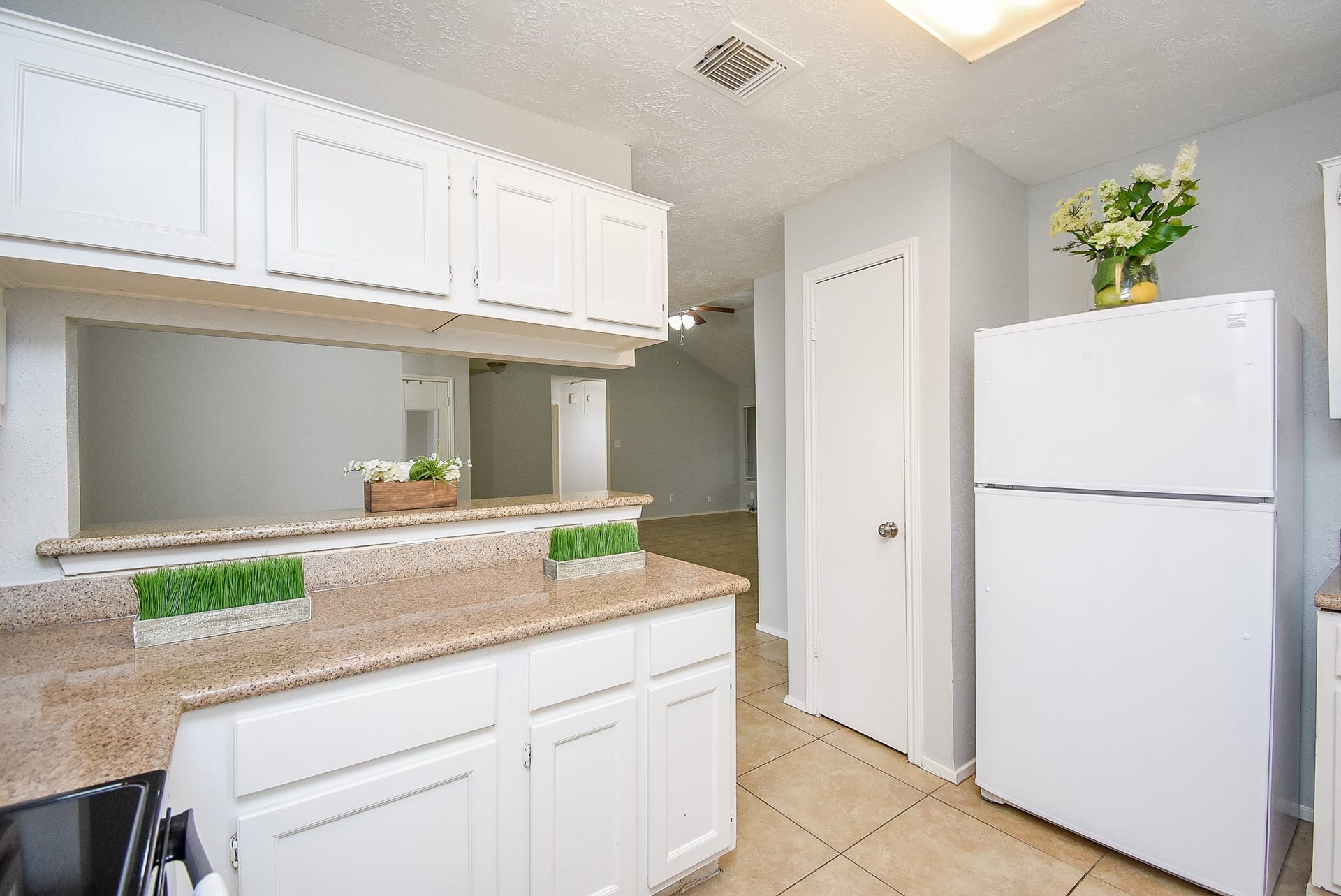 16806 Red Gully Drive, Sugar Land, TX 77498 Bright kitchen with white cabinets and appliances, granite countertops, and tile flooring. The open layout offers a view into the living area.