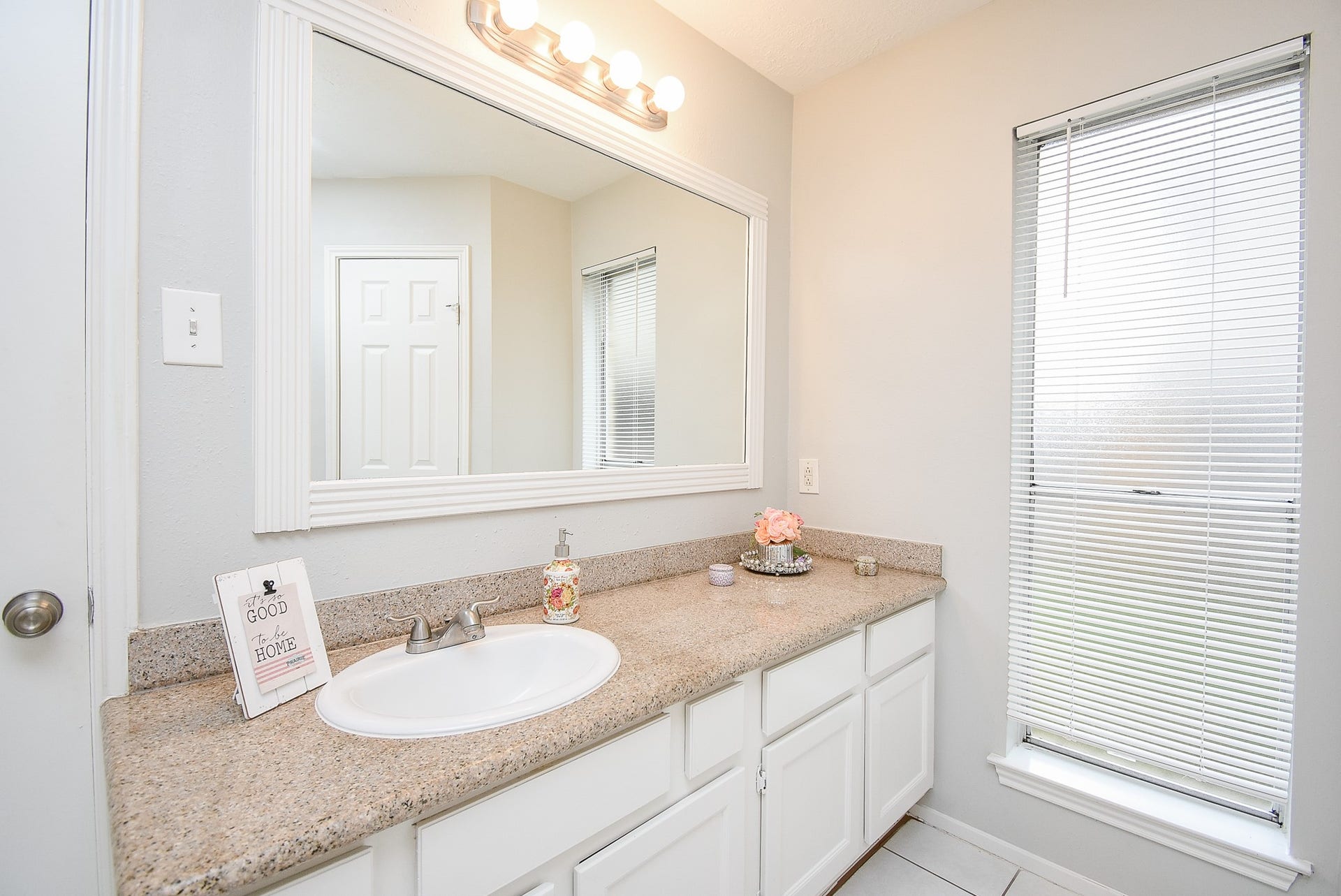 16806 Red Gully Drive, Sugar Land, TX 77498 Bright and modern bathroom with a large mirror, granite countertop, and ample storage below. Natural light streams in through a window with blinds, creating an inviting atmosphere.