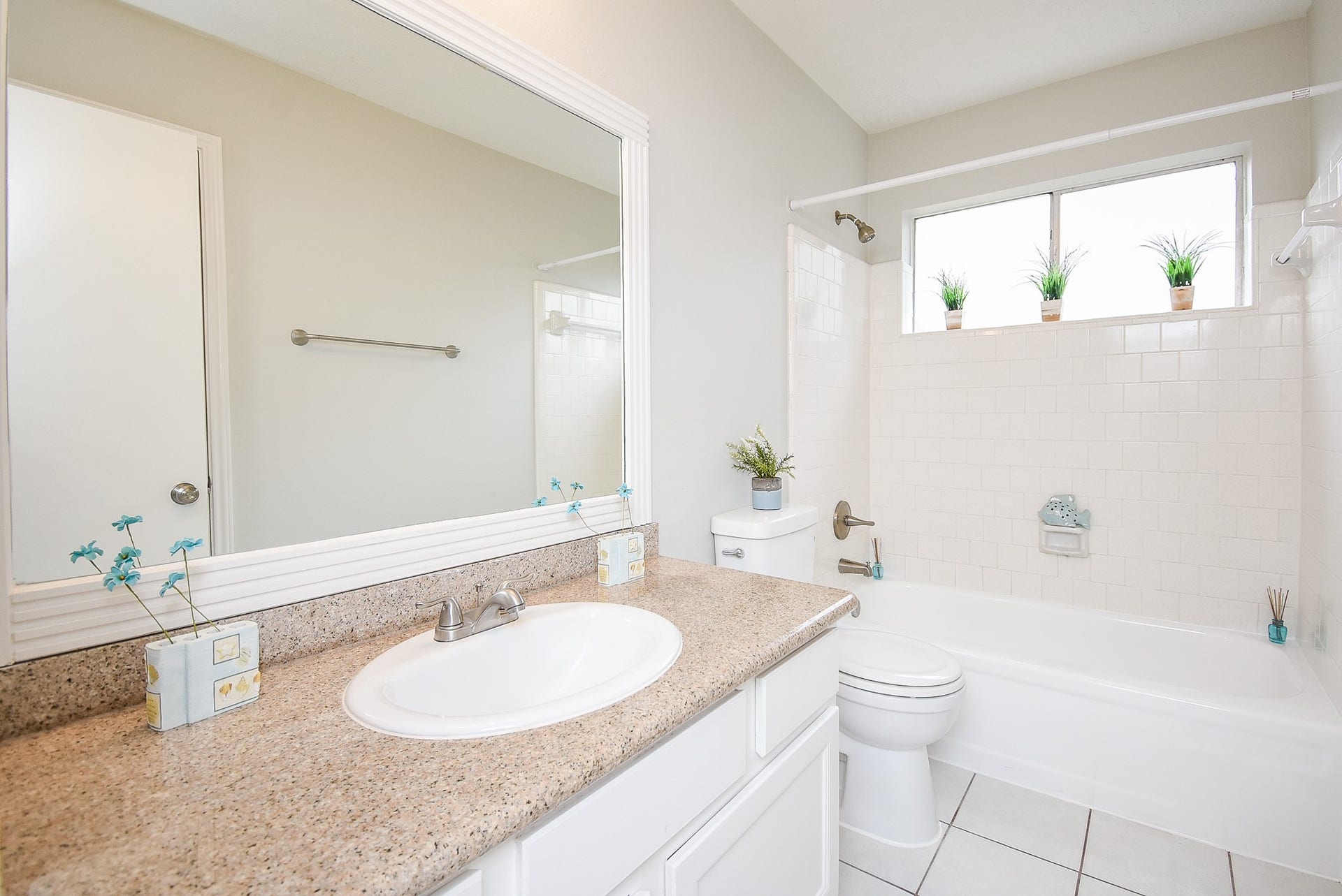 16806 Red Gully Drive, Sugar Land, TX 77498 Bright bathroom with a sleek granite countertop, a large mirror, and a clean white bathtub. The room features a window that lets in natural light, with small plants adding a touch of greenery.