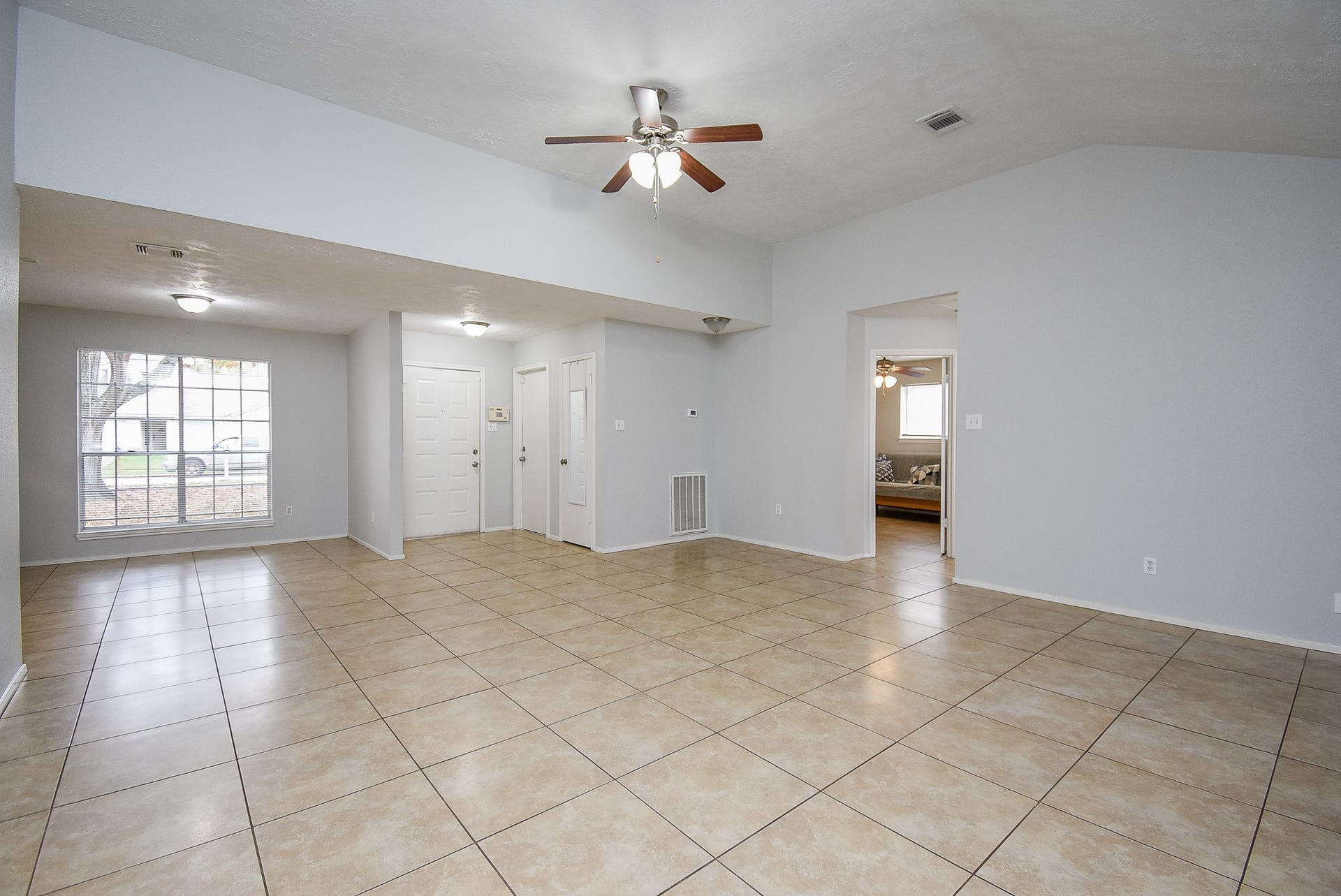 16806 Red Gully Drive, Sugar Land, TX 77498 Spacious living area with neutral tile flooring, ceiling fans, and ample natural light from a large window. The open layout offers versatility, and there's access to adjacent rooms.