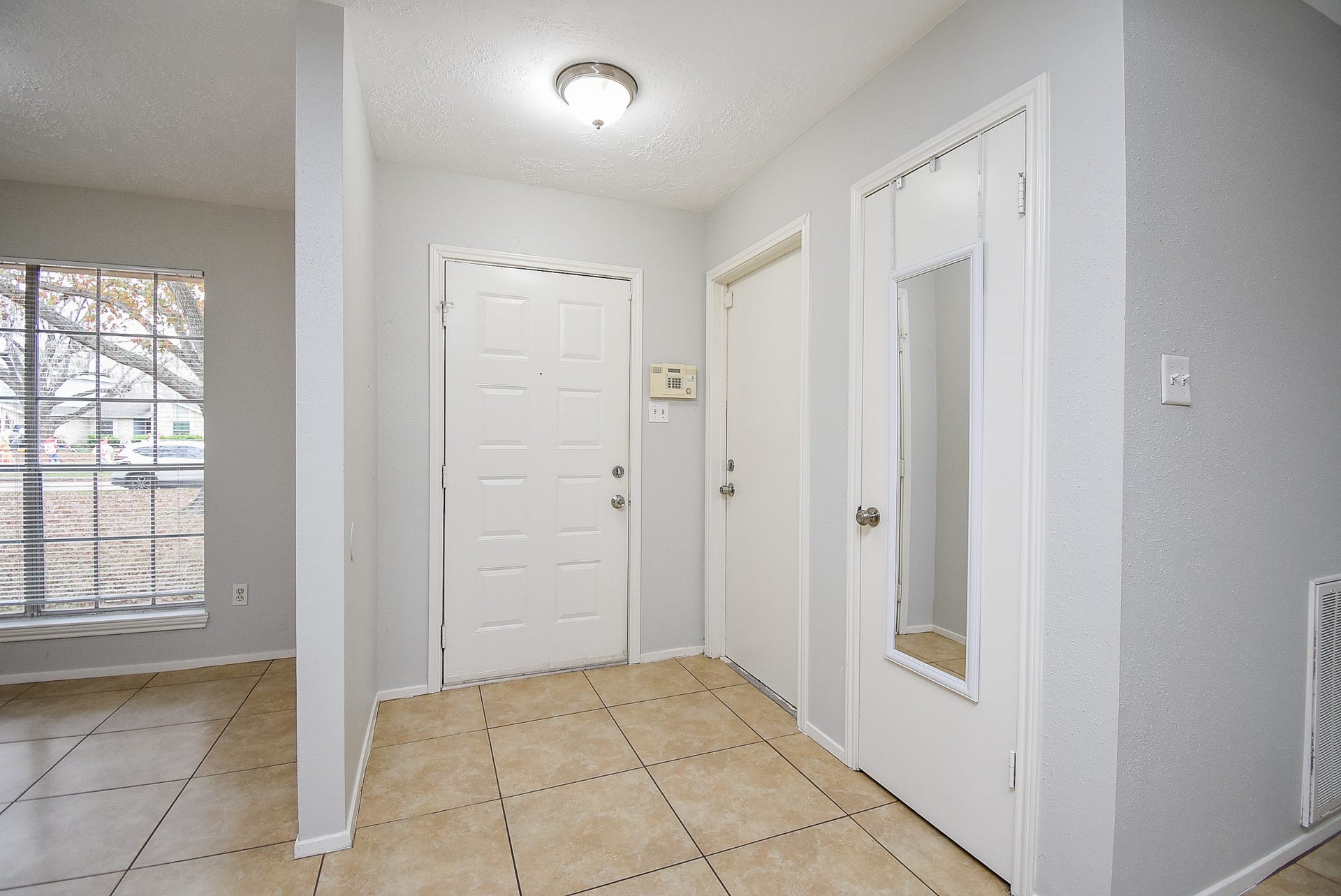 16806 Red Gully Drive, Sugar Land, TX 77498 This entryway features neutral tile flooring, light gray walls, and a large window for natural light. It includes a main door, closet, and a full-length mirror, creating a bright and welcoming space.