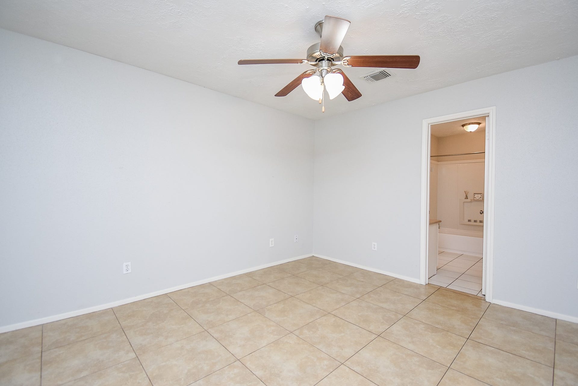 16806 Red Gully Drive, Sugar Land, TX 77498 This photo shows a clean, spacious bedroom with tiled flooring, a ceiling fan, and a neutral color scheme. It features an ensuite bathroom with a tiled floor, adding convenience and privacy.