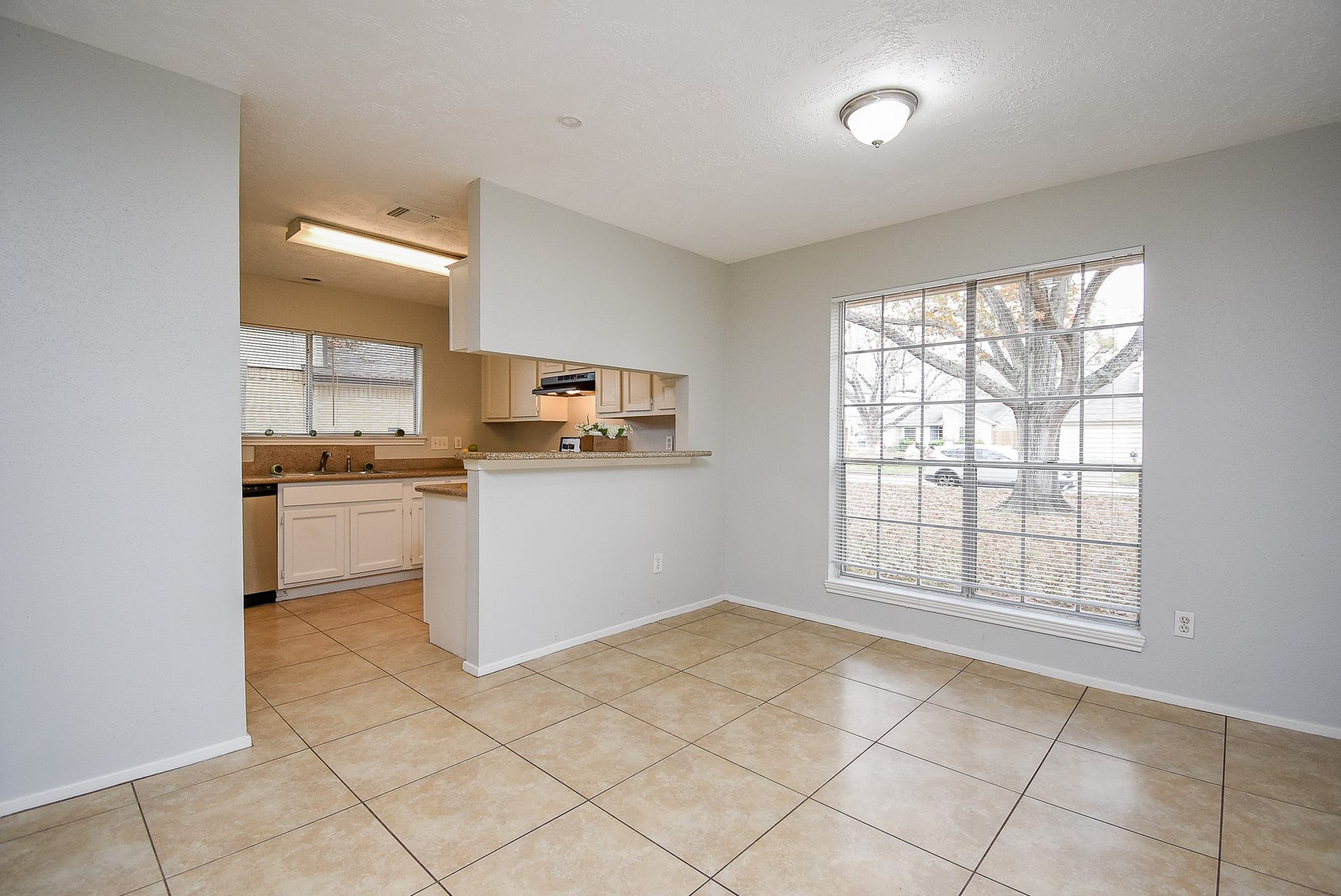 16806 Red Gully Drive, Sugar Land, TX 77498 This photo shows a bright, open kitchen and dining area with tiled floors and a large window providing ample natural light. The kitchen features white cabinetry and a cutout for easy interaction with the dining space.