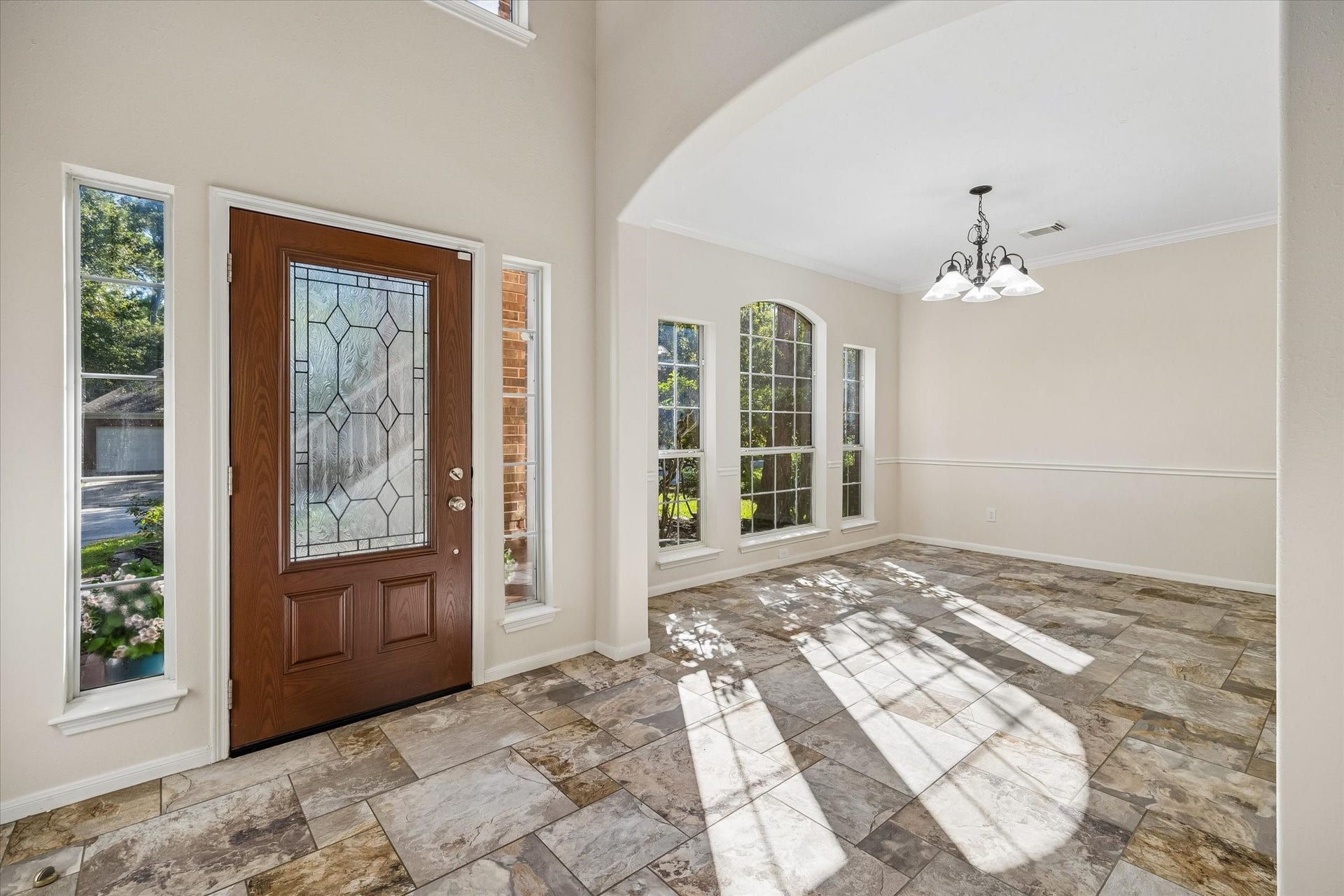 11 Merryvale Drive, The Woodlands, TX 77382 The entry opens into a bright, inviting space with large windows, natural light, and an elegant arched opening leading into the dining area.