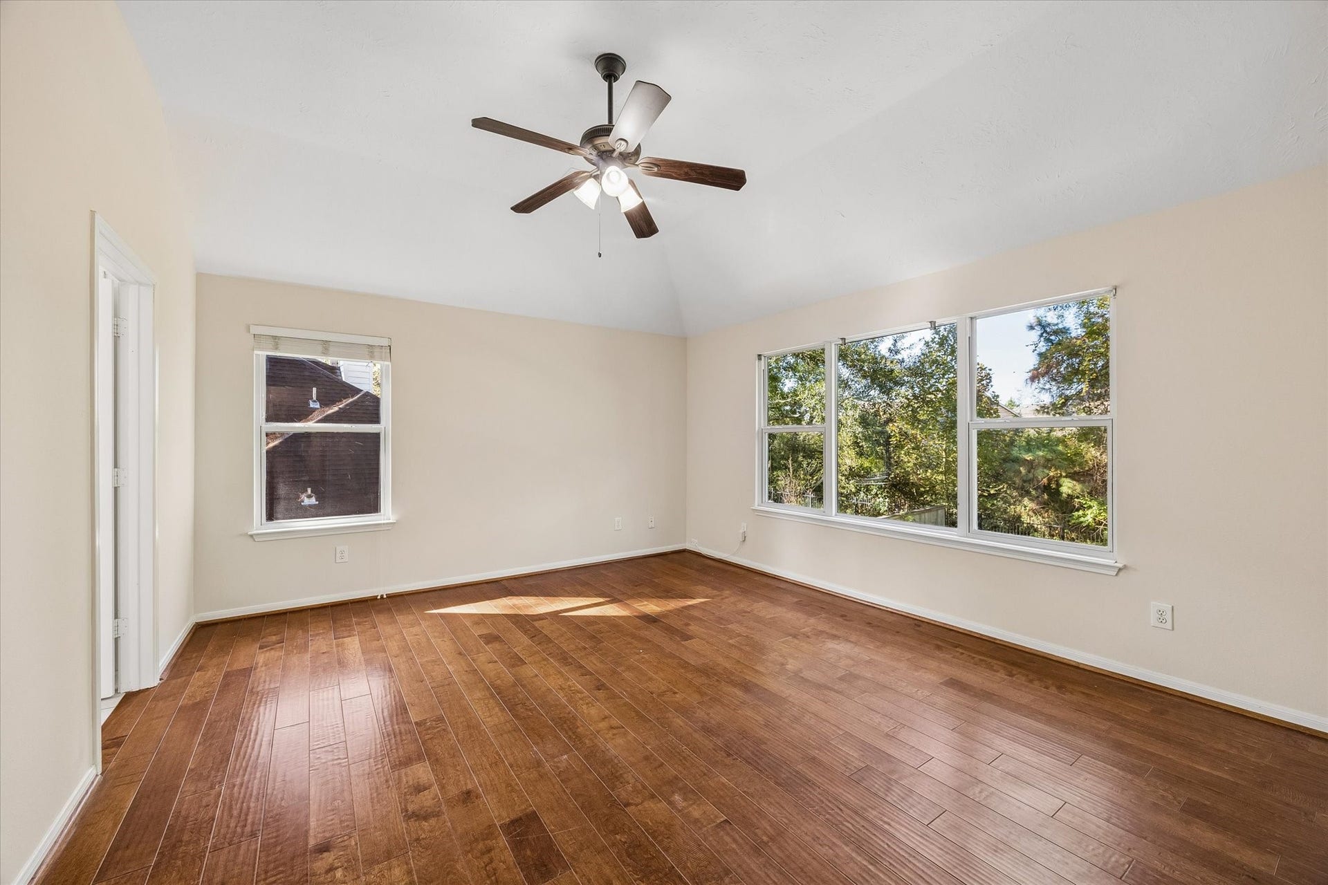 11 Merryvale Drive, The Woodlands, TX 77382 Spacious second-level primary bedroom featuring engineered wood flooring and expansive windows that fill the room with natural light while offering peaceful views of the surrounding greenery.