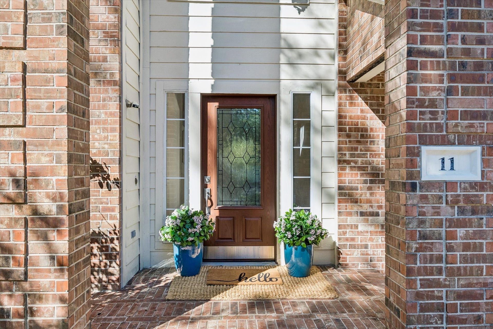 11 Merryvale Drive, The Woodlands, TX 77382 Step inside through the welcoming entryway, featuring a beautiful custom wood front door with decorative glass, framed by classic brick accents.