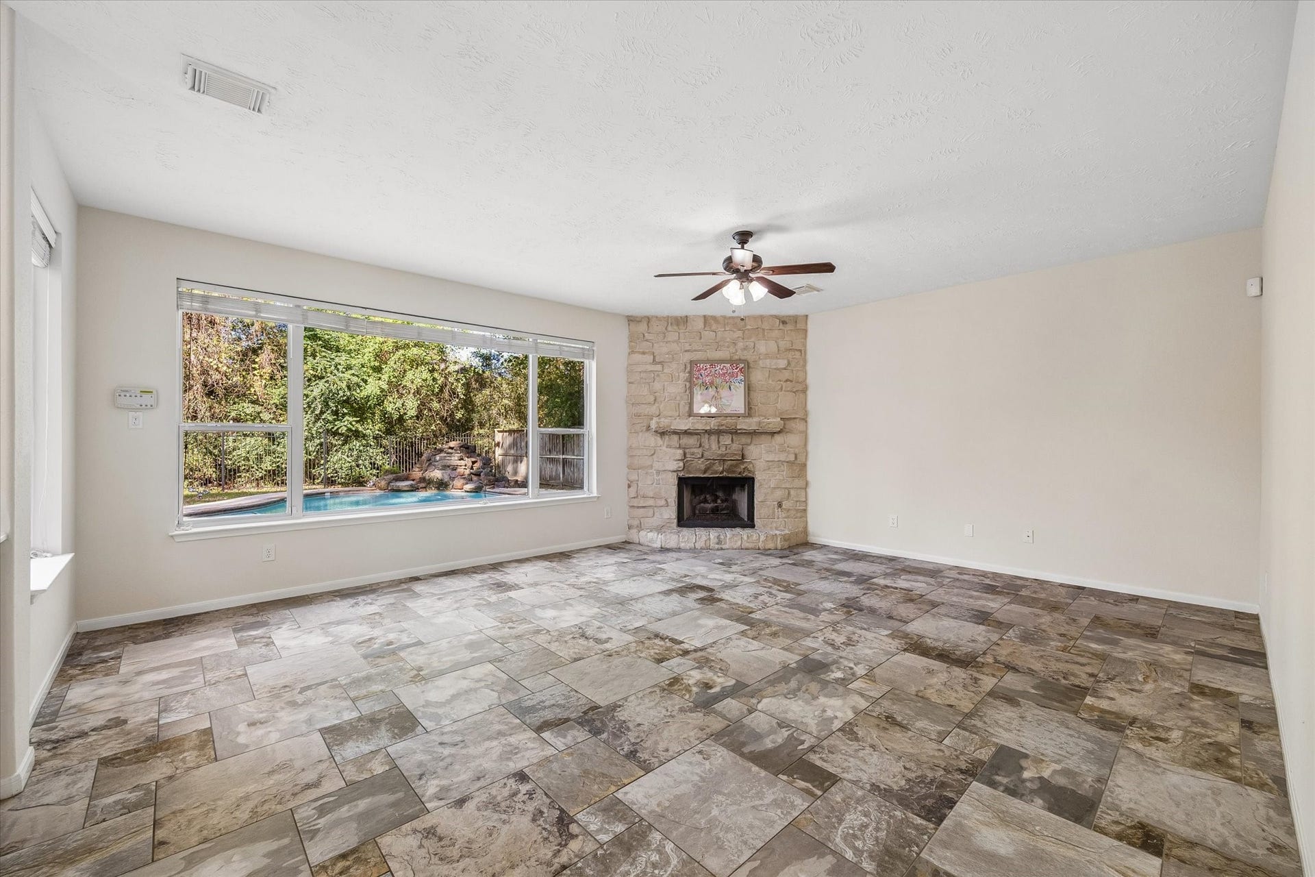 11 Merryvale Drive, The Woodlands, TX 77382 Spacious living area featuring a beautiful stone fireplace, expansive windows overlooking the backyard and pool, and an abundance of natural light. Floors and light fixtures have been updated in this home!