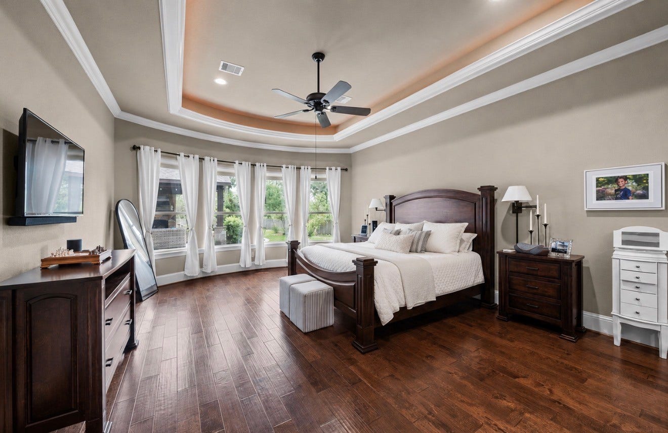 4426 Silver Jade Drive, Spring, TX 77386 Your private main-level sanctuary. The grand primary suite is a masterclass in refined comfort, boasting rich hardwood underfoot and a dramatic wall of sweeping bay windows that bathes the space in a soft, ethereal morning glow.