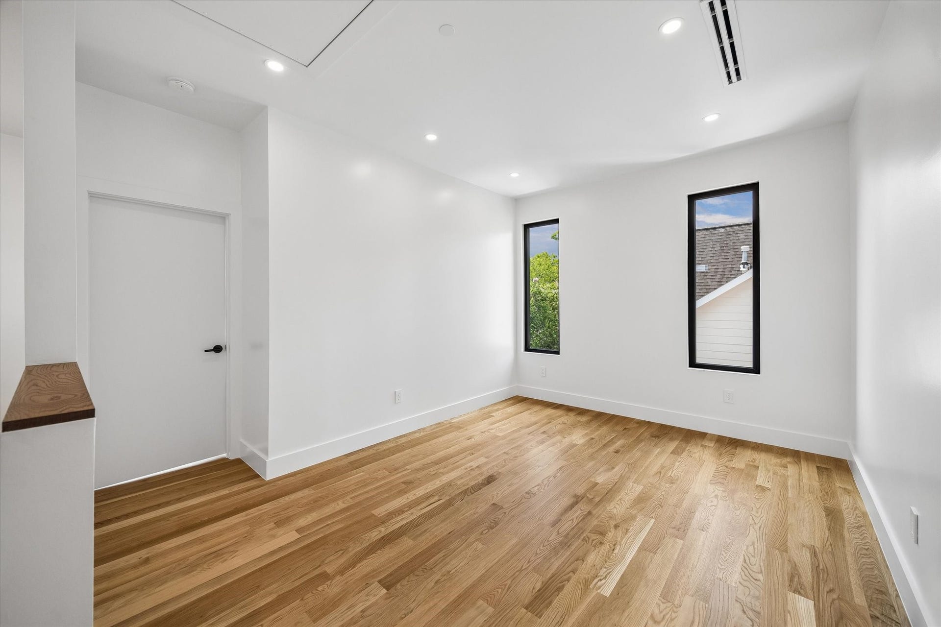 Bright and inviting room featuring hardwood floors, fresh white walls, and two tall windows offering ample natural light.