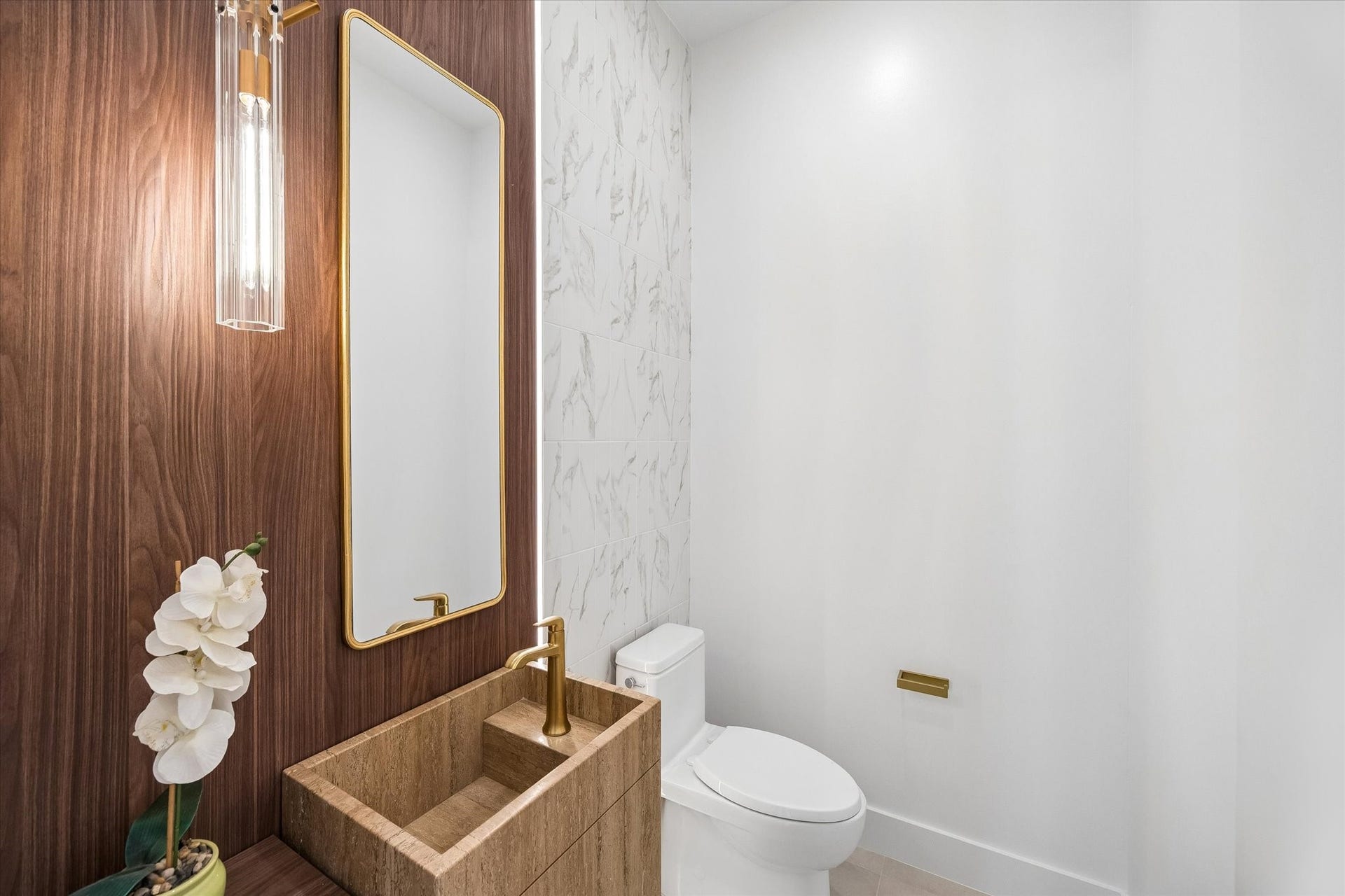 Elegant powder room featuring a custom made Travertine sink, accented by a modern gold-framed mirror and stylish lighting.