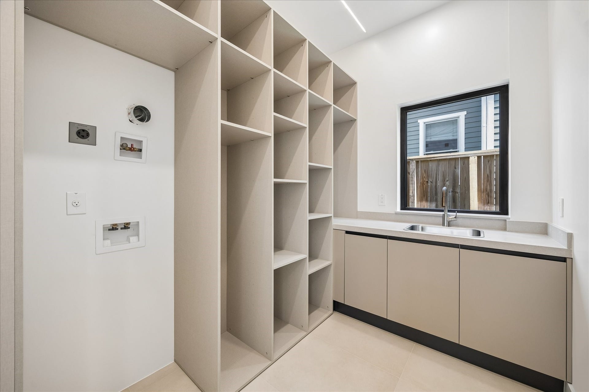 Modern utility room featuring ample storage with open shelving, a sleek countertop with an integrated sink, and a large window for natural light.