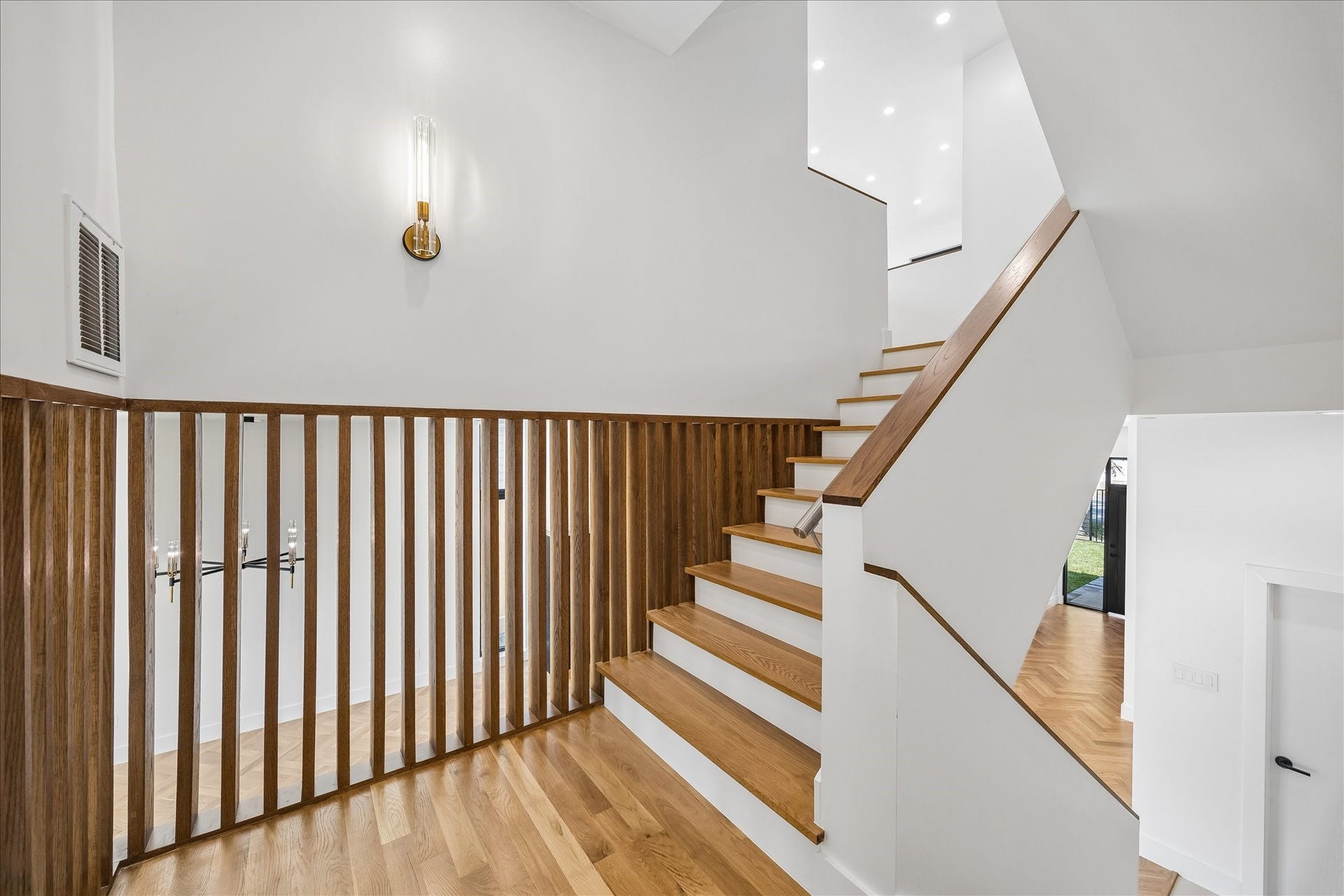 A modern staircase with elegant wood accents and sleek white walls, featuring contemporary lighting and an open design.