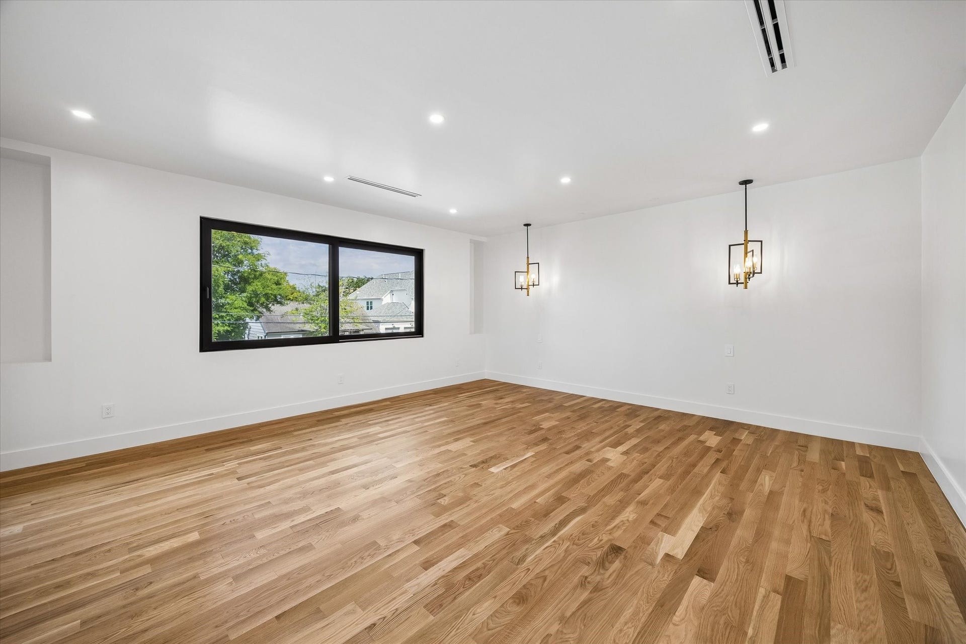 Primary bedroom featuring sleek hardwood floors, modern pendant lighting, and a large window offering natural light and scenic views.