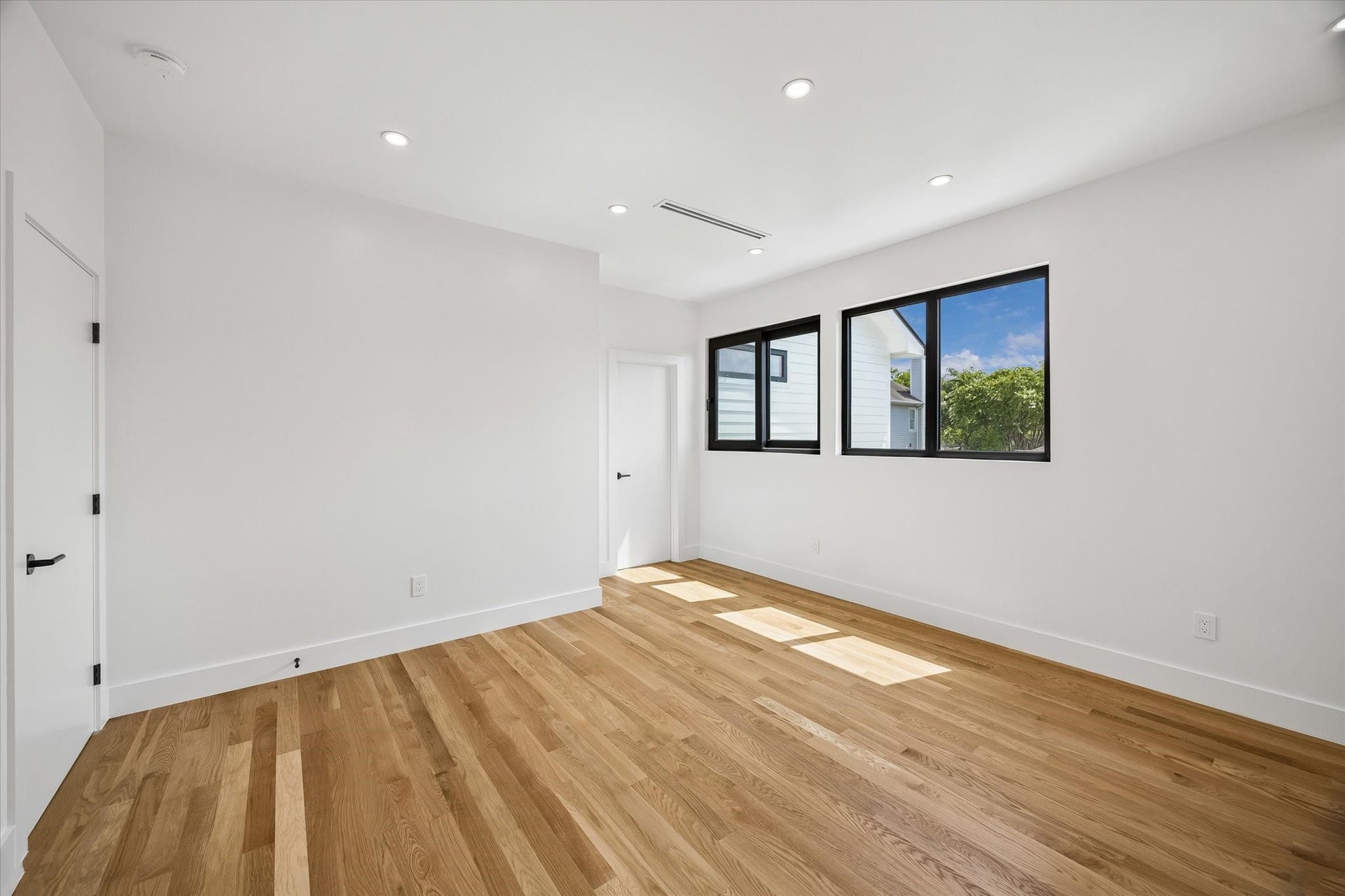 Bright and spacious room with sleek hardwood floors, recessed lighting, and large windows offering abundant natural light.