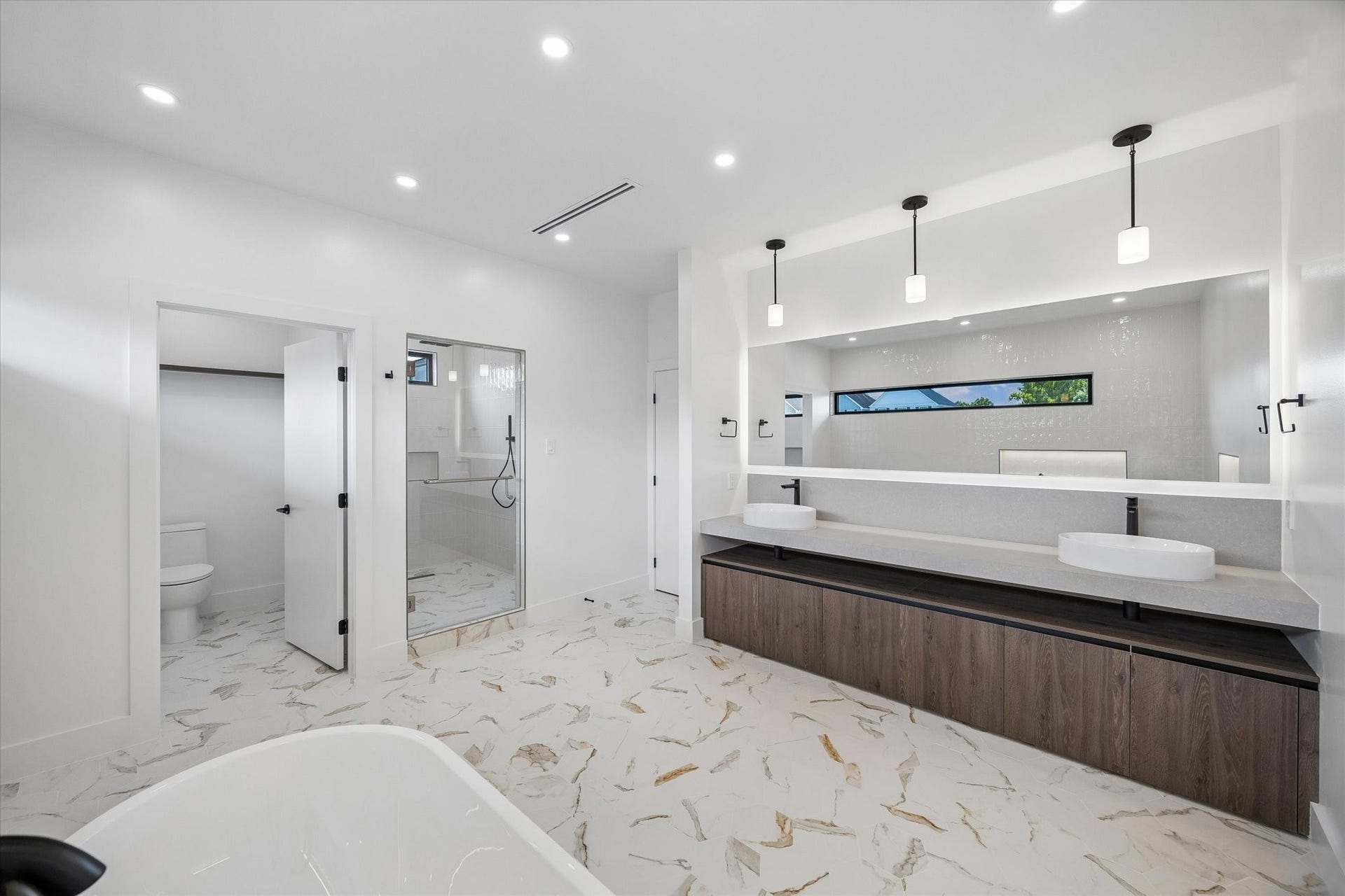 Double vanity with elegant pendant lighting, a walk-in shower, and a separate toilet area, all set on beautiful marble flooring.