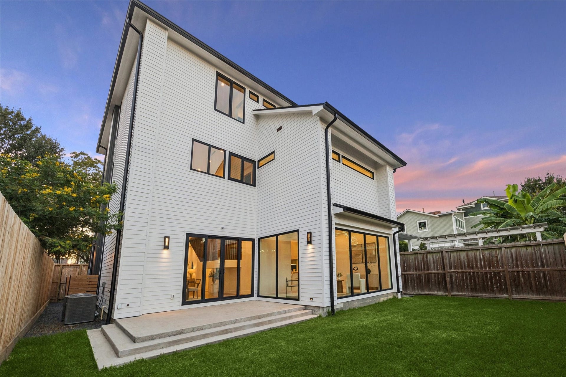 Modern three-story home with sleek white siding, expansive windows, and a spacious backyard, perfect for outdoor entertaining.