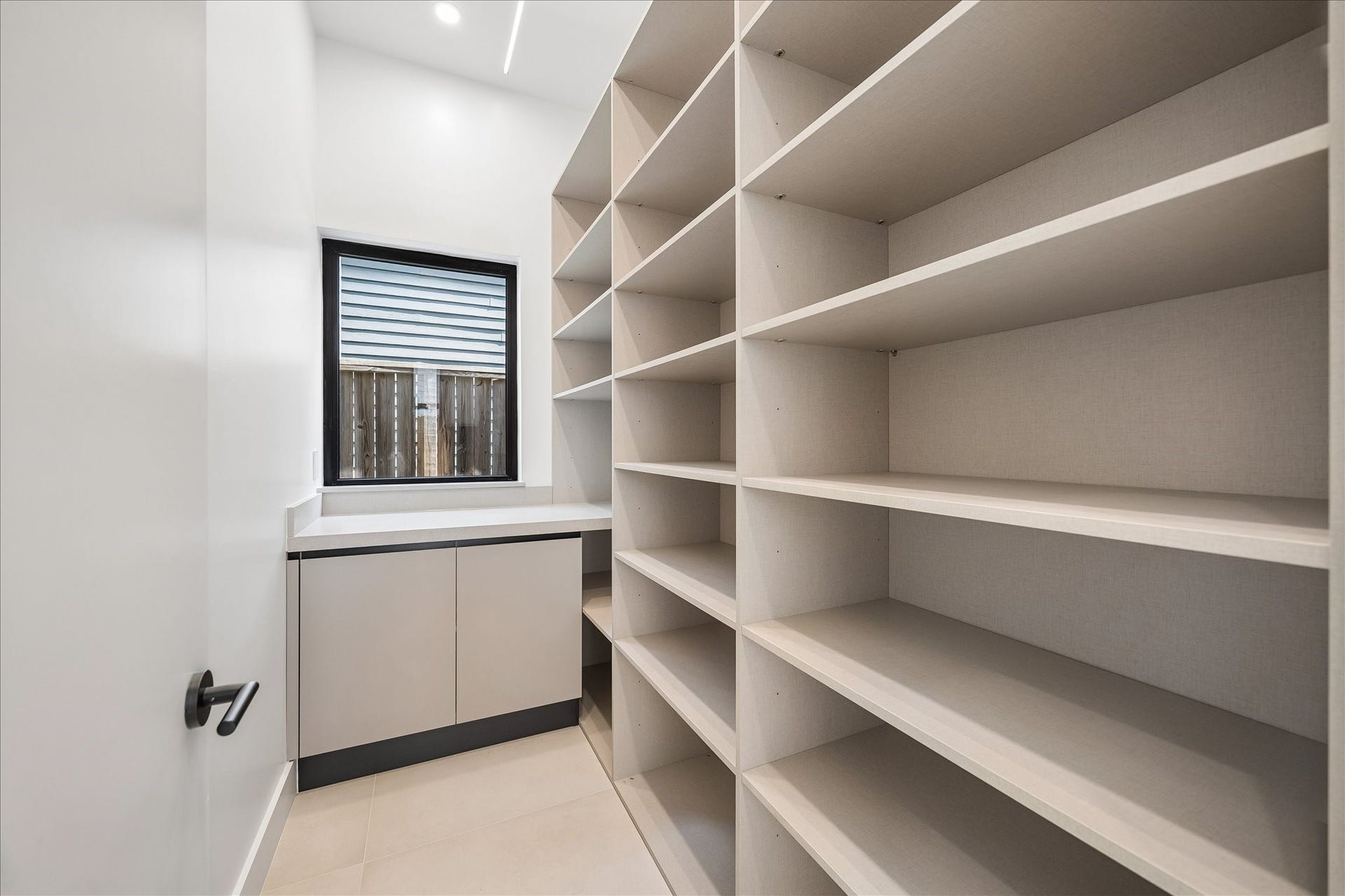 Walk-in pantry with ample shelving and an auxiliary countertop, featuring a window for natural light.