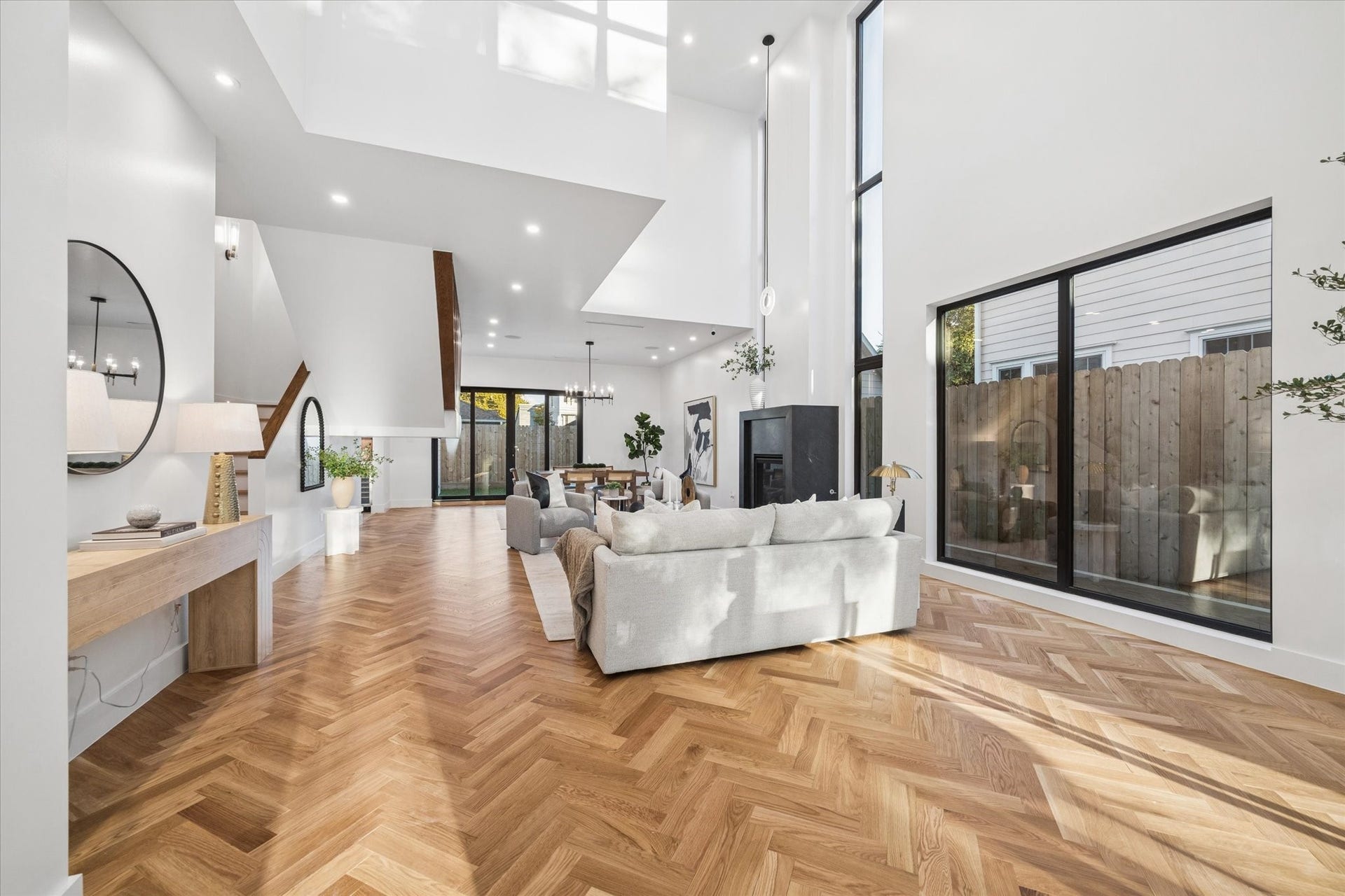 Stunning open-concept living space with soaring ceilings, elegant herringbone wood flooring, and expansive windows that flood the area with natural light.