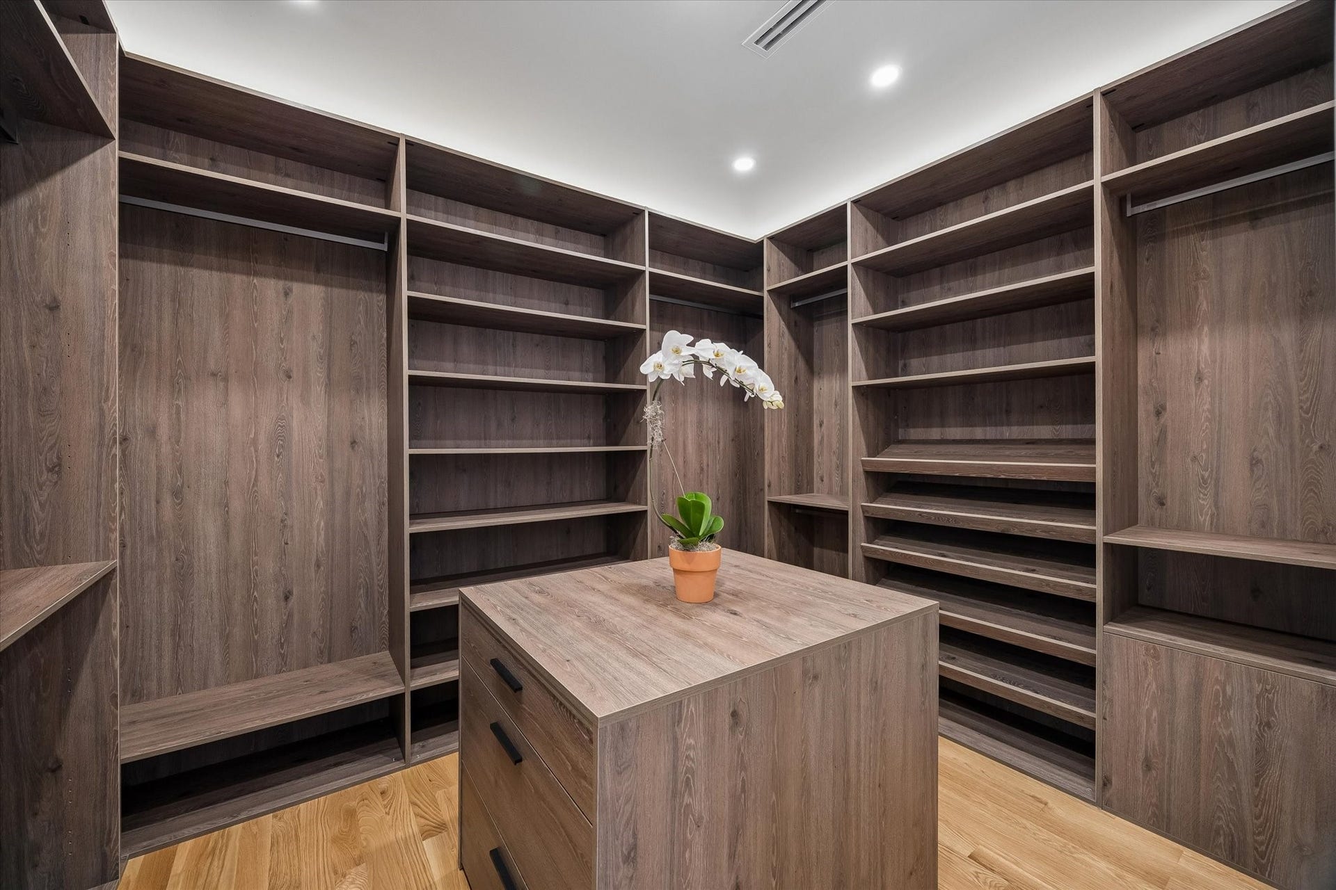Enjoy relaxing on this spacious balcony with elegant wood-tile flooring and a modern glass railing, surrounded by lush greenery for an outdoor escape.