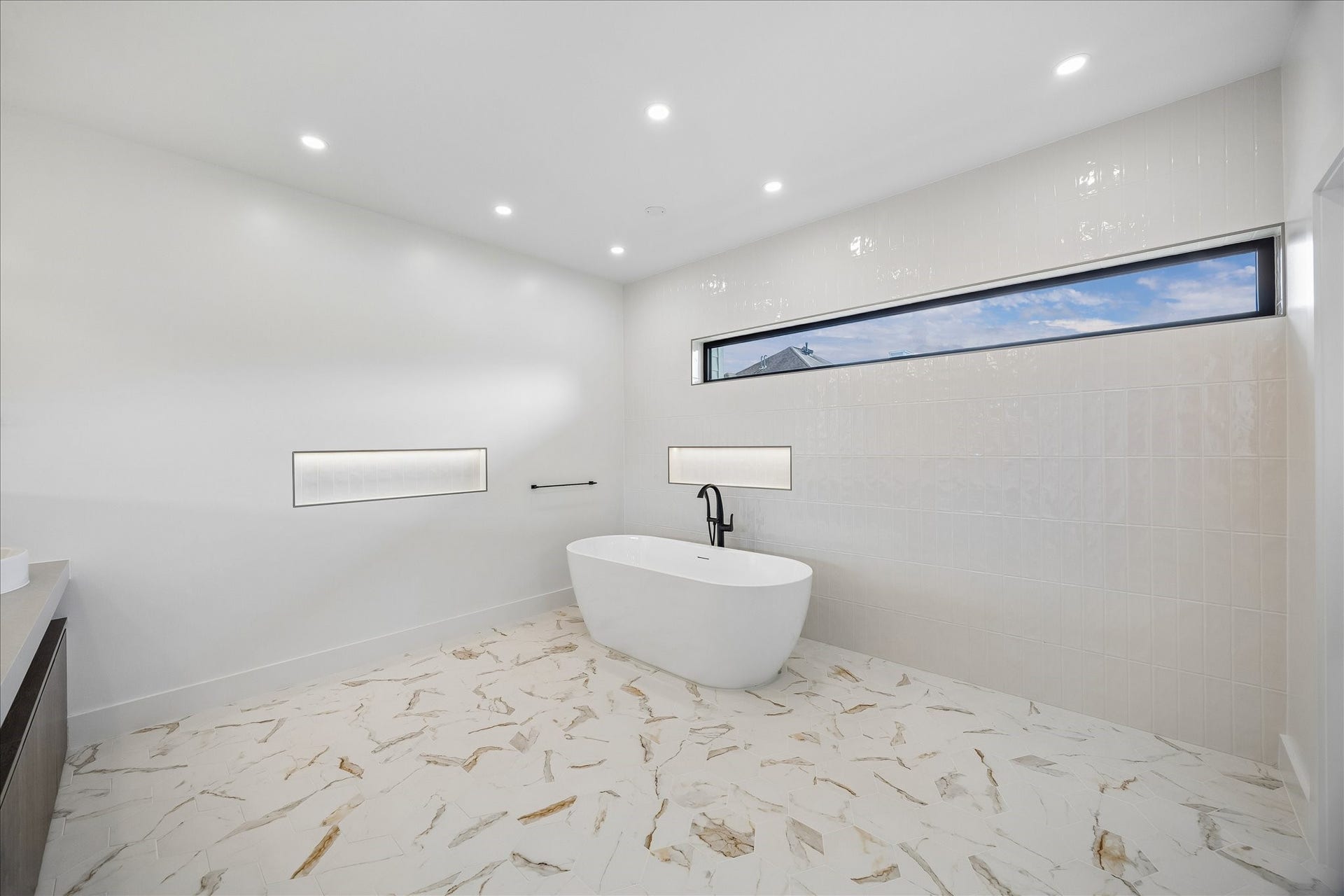 Luxurious bathroom featuring a freestanding tub, elegant tile flooring, and modern recessed lighting, complemented by a stylish horizontal window for natural light.