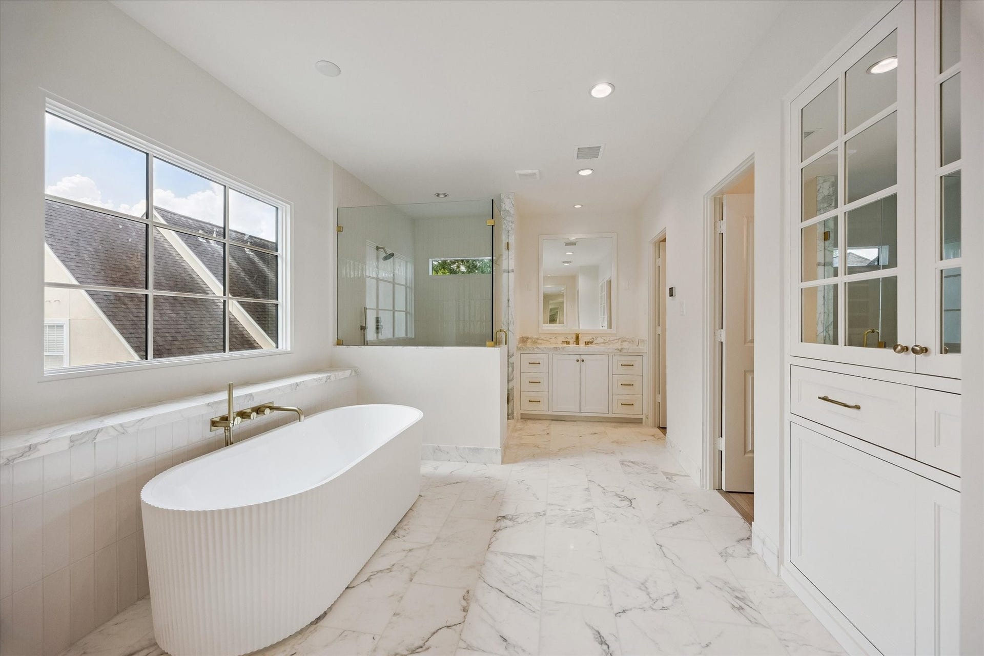Serene and spacious primary bath with Calacatta Gold countertops and tile, fluted soaking tub, large walk-in shower, and his/hers closets.  Sconce lighting not yet installed.