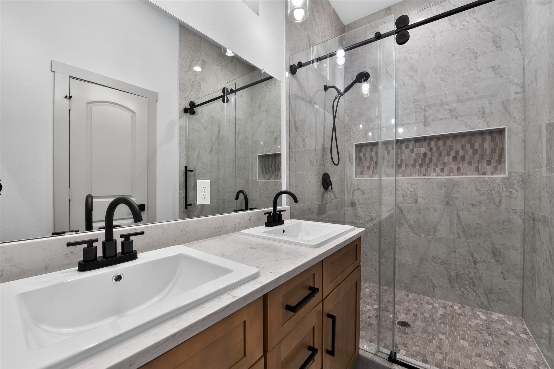 The primary bath features dual sinks, abundant storage, and an oversized walk-in shower with floor-to-ceiling tile and seamless glass doors.