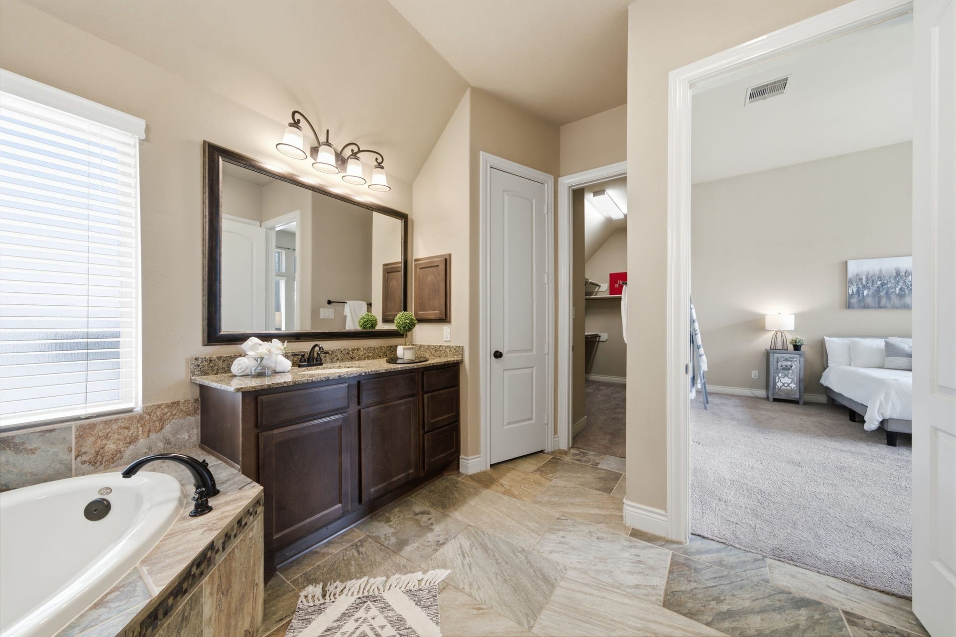 4603 Piper Shadow Lane, Katy, TX 77494 Elegant bathroom with a luxurious corner bathtub, granite-topped dual vanity, and stylish lighting, leading into a cozy, carpeted bedroom.