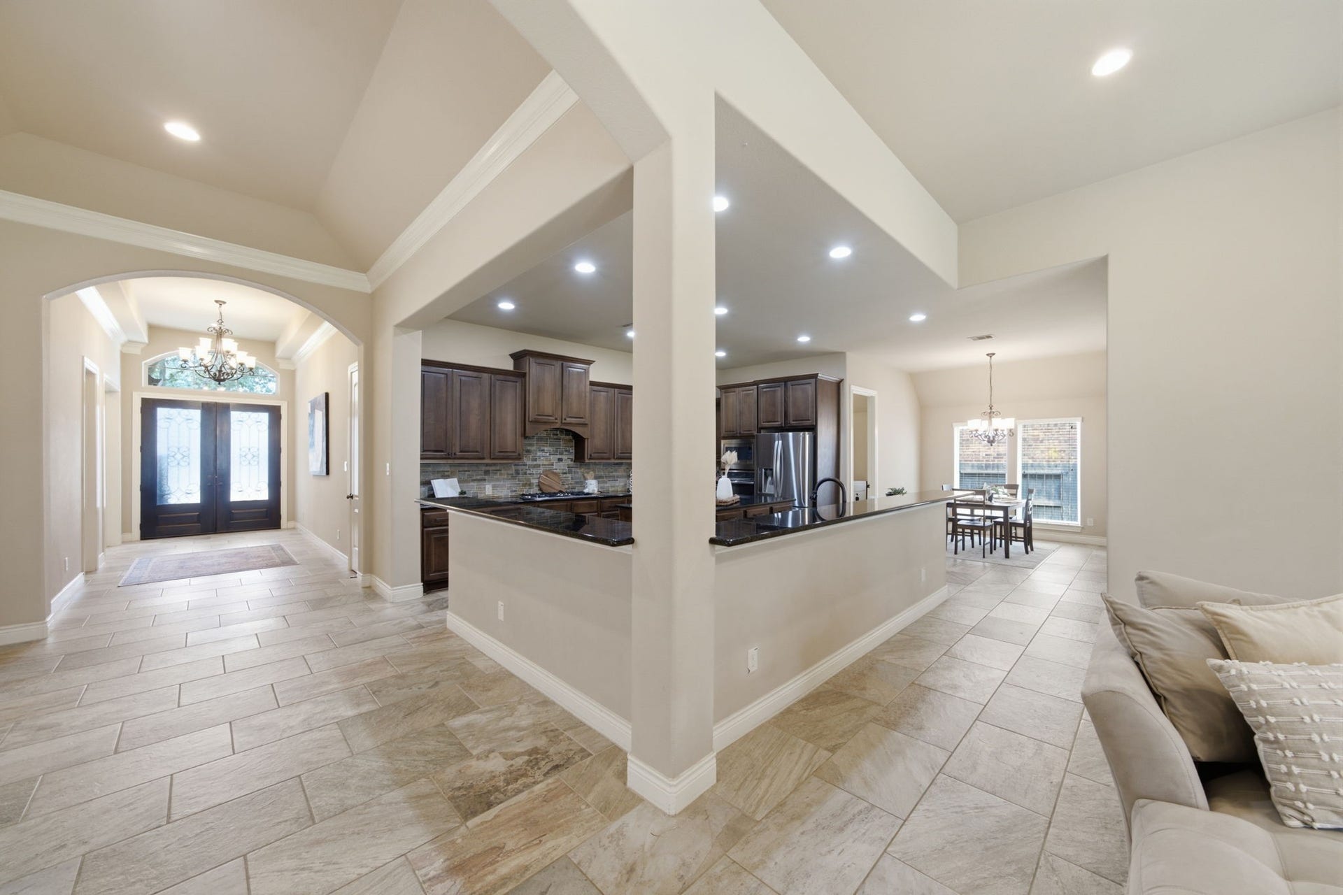 4603 Piper Shadow Lane, Katy, TX 77494 Elegant open-concept layout featuring a spacious entryway with a chandelier, leading to a modern kitchen with dark wood cabinetry and granite countertops, seamlessly flowing into a bright dining area.