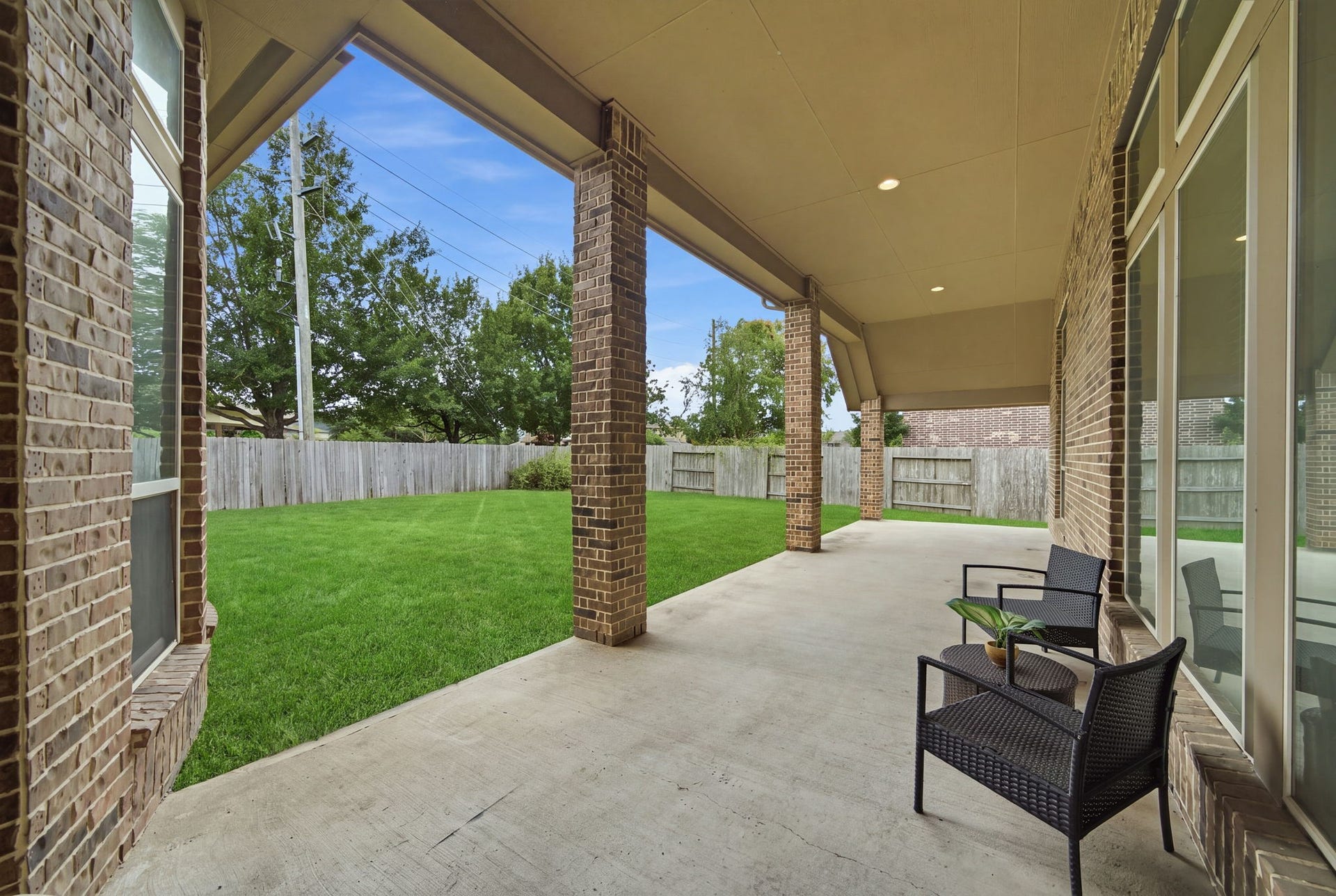 4603 Piper Shadow Lane, Katy, TX 77494 Spacious covered patio with elegant brick columns opens to a lush, fenced backyard, perfect for outdoor relaxation and entertaining.