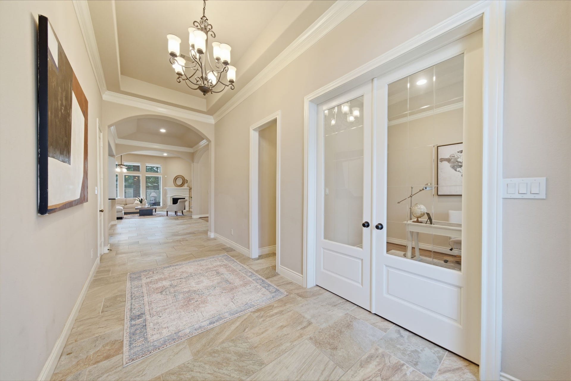 4603 Piper Shadow Lane, Katy, TX 77494 Elegant entryway with a high ceiling, stylish chandelier, and beautiful tile flooring leading to an inviting living area. A pair of glass French doors open to a cozy home office.