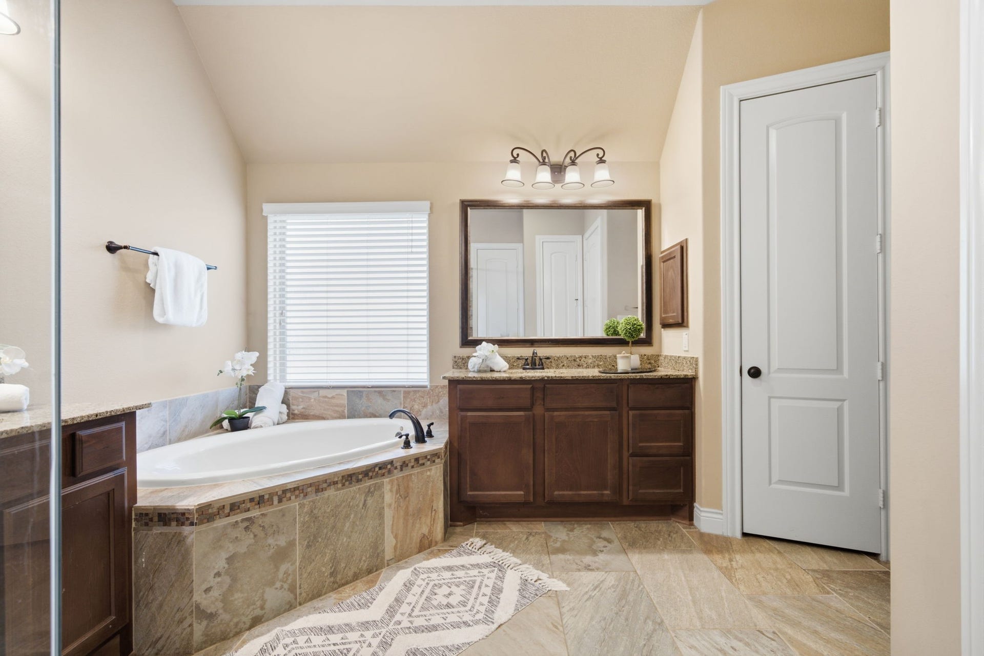 4603 Piper Shadow Lane, Katy, TX 77494 Elegant bathroom featuring a luxurious soaking tub, dual-sink vanity with granite countertops, and a large mirror, complemented by warm wood cabinetry and stylish lighting.