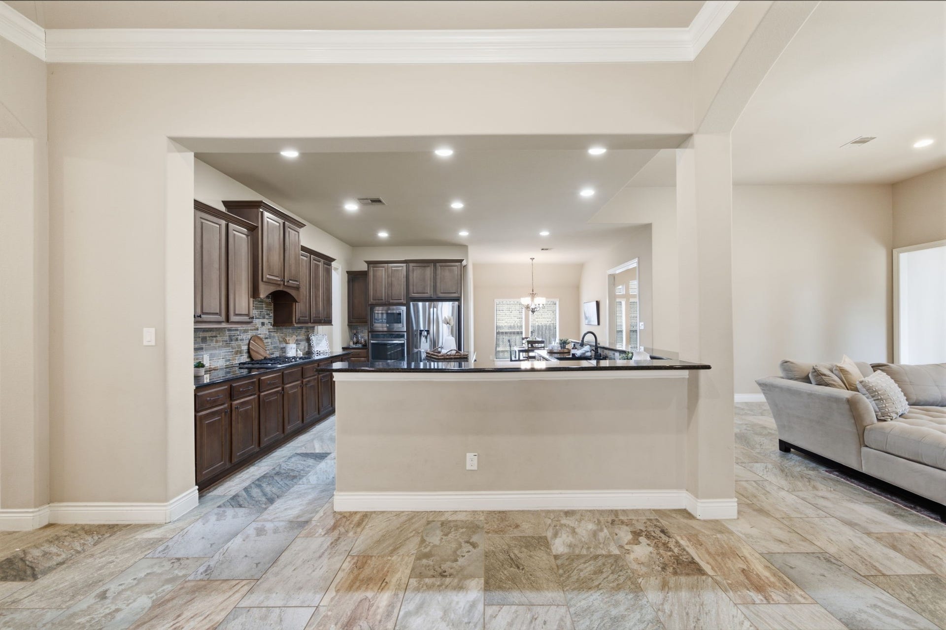 4603 Piper Shadow Lane, Katy, TX 77494 Spacious open-concept kitchen with elegant dark wood cabinetry, granite countertops, and a sleek tile backsplash, seamlessly flowing into a cozy living area with ample natural light.