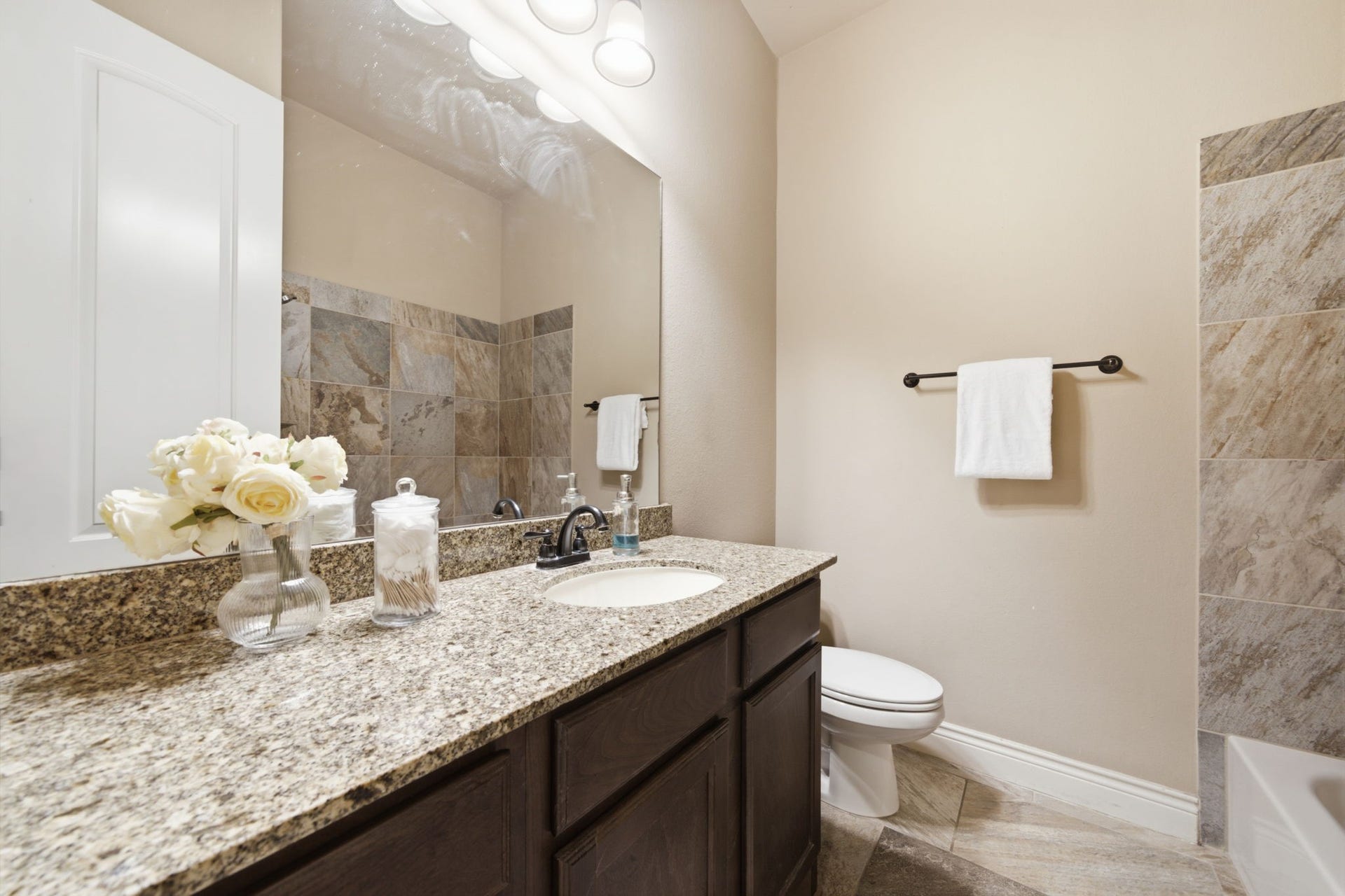 4603 Piper Shadow Lane, Katy, TX 77494 Elegant bathroom featuring a granite countertop, rich dark cabinetry, and a beautifully tiled shower, complemented by soft lighting and stylish fixtures.