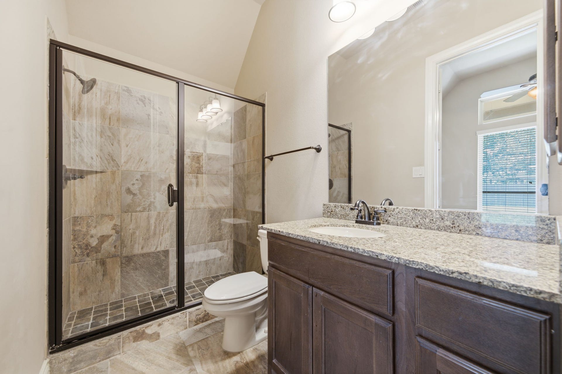 4603 Piper Shadow Lane, Katy, TX 77494 Elegant bathroom featuring a spacious glass-enclosed shower with stone tile, a sleek granite countertop, and rich dark wood cabinetry.