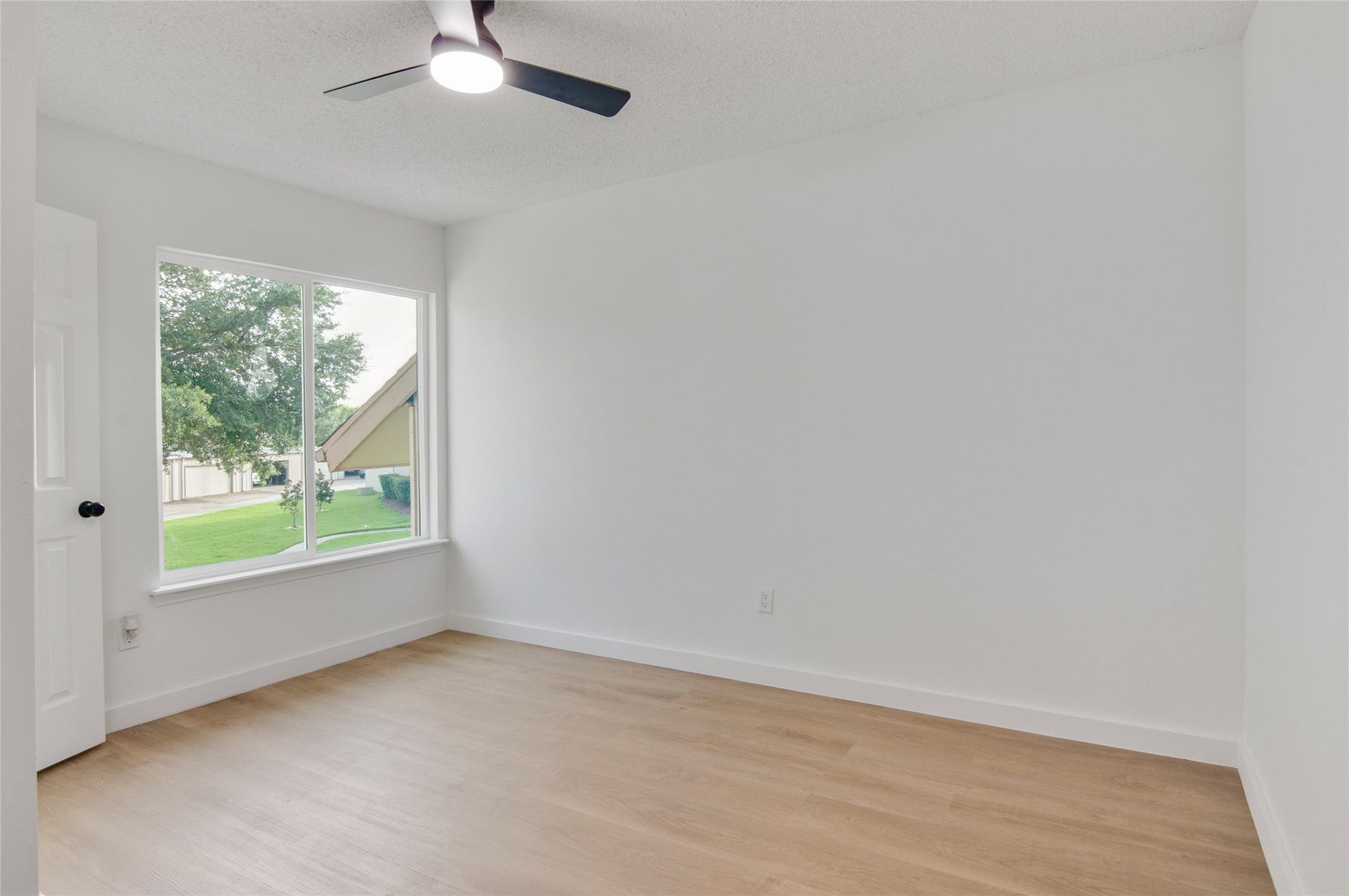 2916 Windchase Blvd, Houston, TX 77082 Bright and airy room featuring sleek laminate flooring, a modern ceiling fan, and a large window with a serene view of lush greenery.