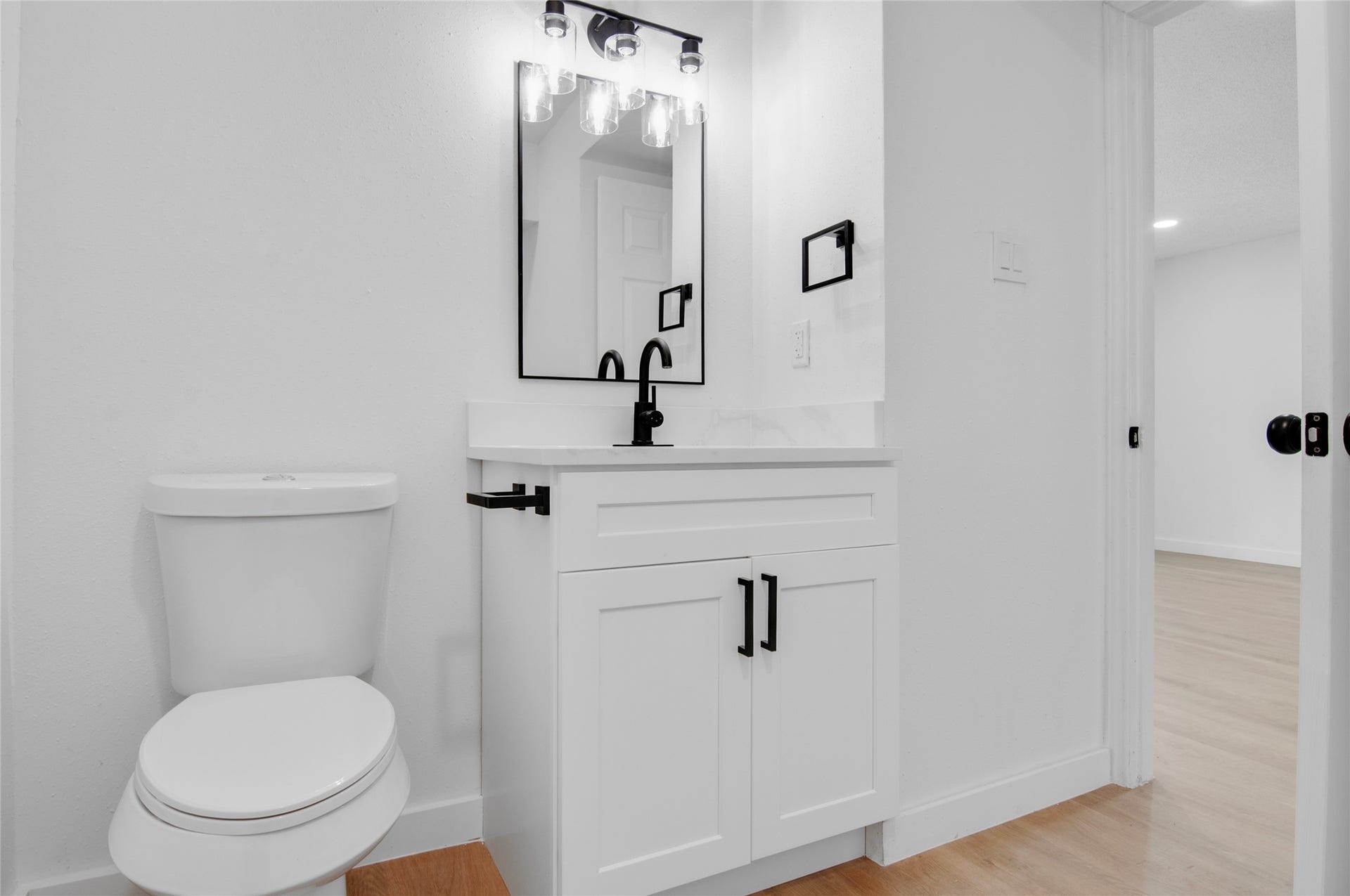 2916 Windchase Blvd, Houston, TX 77082 Stylish bathroom with a modern vanity featuring sleek black fixtures, a framed mirror, and pristine white cabinetry, complemented by light wood flooring.