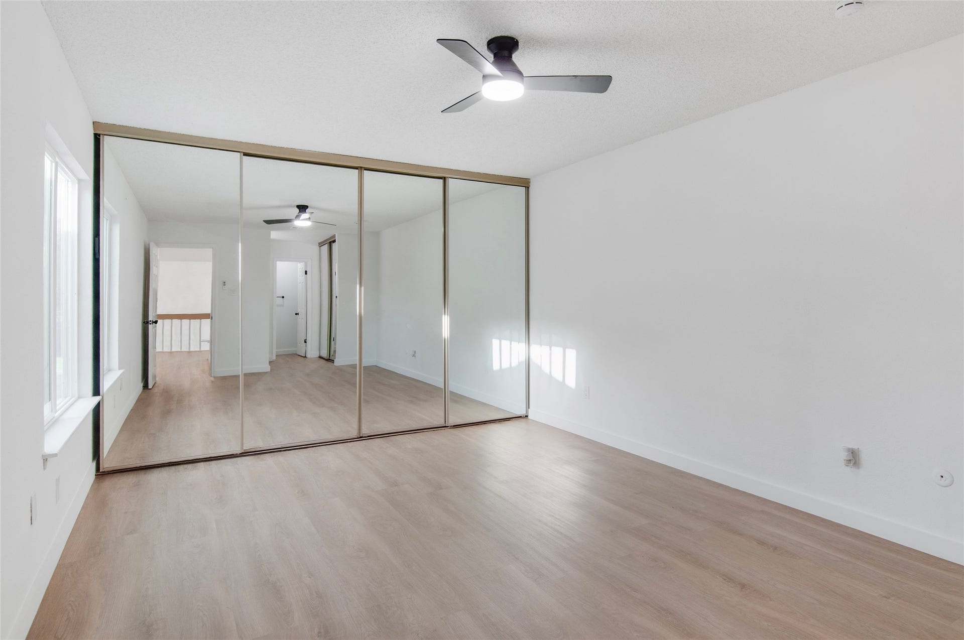 2916 Windchase Blvd, Houston, TX 77082 Spacious bedroom with light wood flooring, mirrored closet doors, and a modern ceiling fan, offering ample natural light.