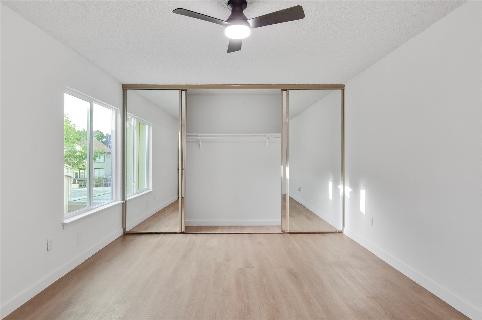 2916 Windchase Blvd, Houston, TX 77082 Bright bedroom featuring sleek mirrored closet doors, modern ceiling fan, and abundant natural light from large windows.