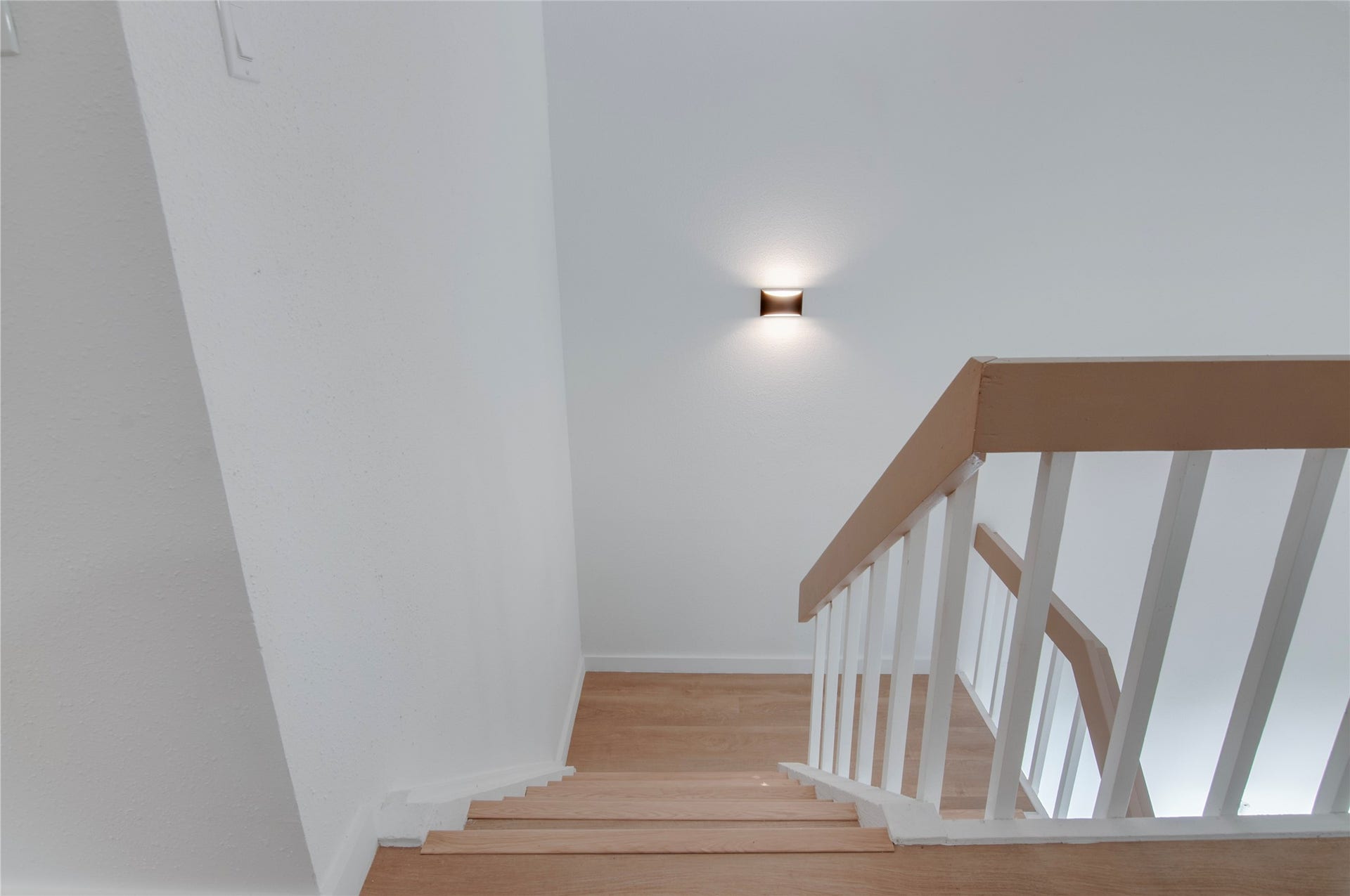 2916 Windchase Blvd, Houston, TX 77082 Modern staircase with sleek wooden steps and white railing, enhanced by a stylish wall-mounted light fixture.