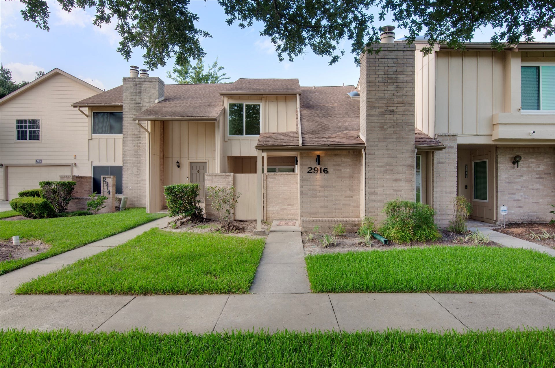 2916 Windchase Blvd, Houston, TX 77082 Charming two-story townhouse with a brick facade and a welcoming front entrance, surrounded by lush greenery and shaded by mature trees.