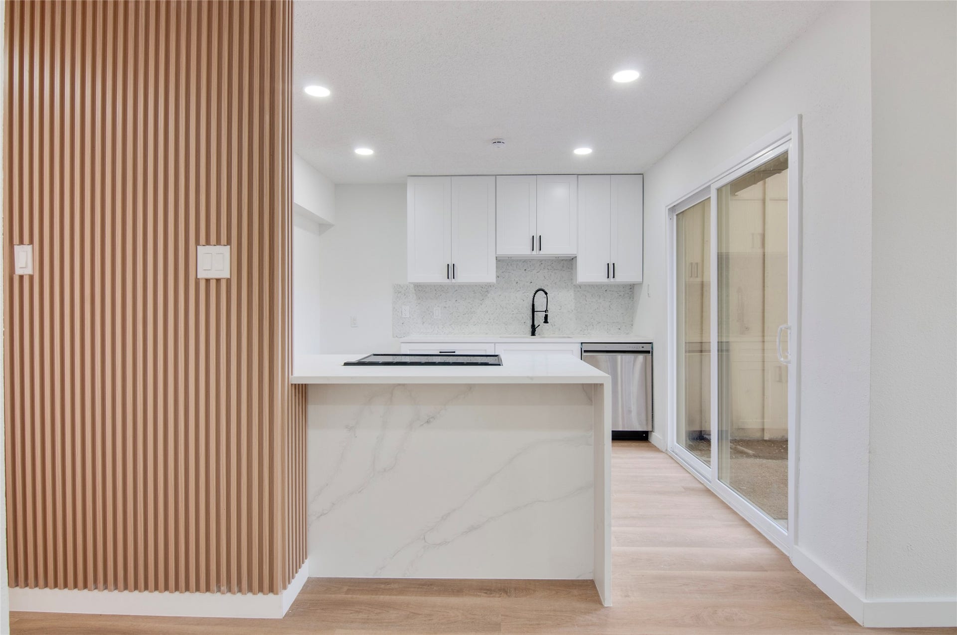 2916 Windchase Blvd, Houston, TX 77082 Modern kitchen featuring sleek cabinetry, a stylish island with marble accents, and stainless steel appliances, enhanced by natural light from sliding glass doors.