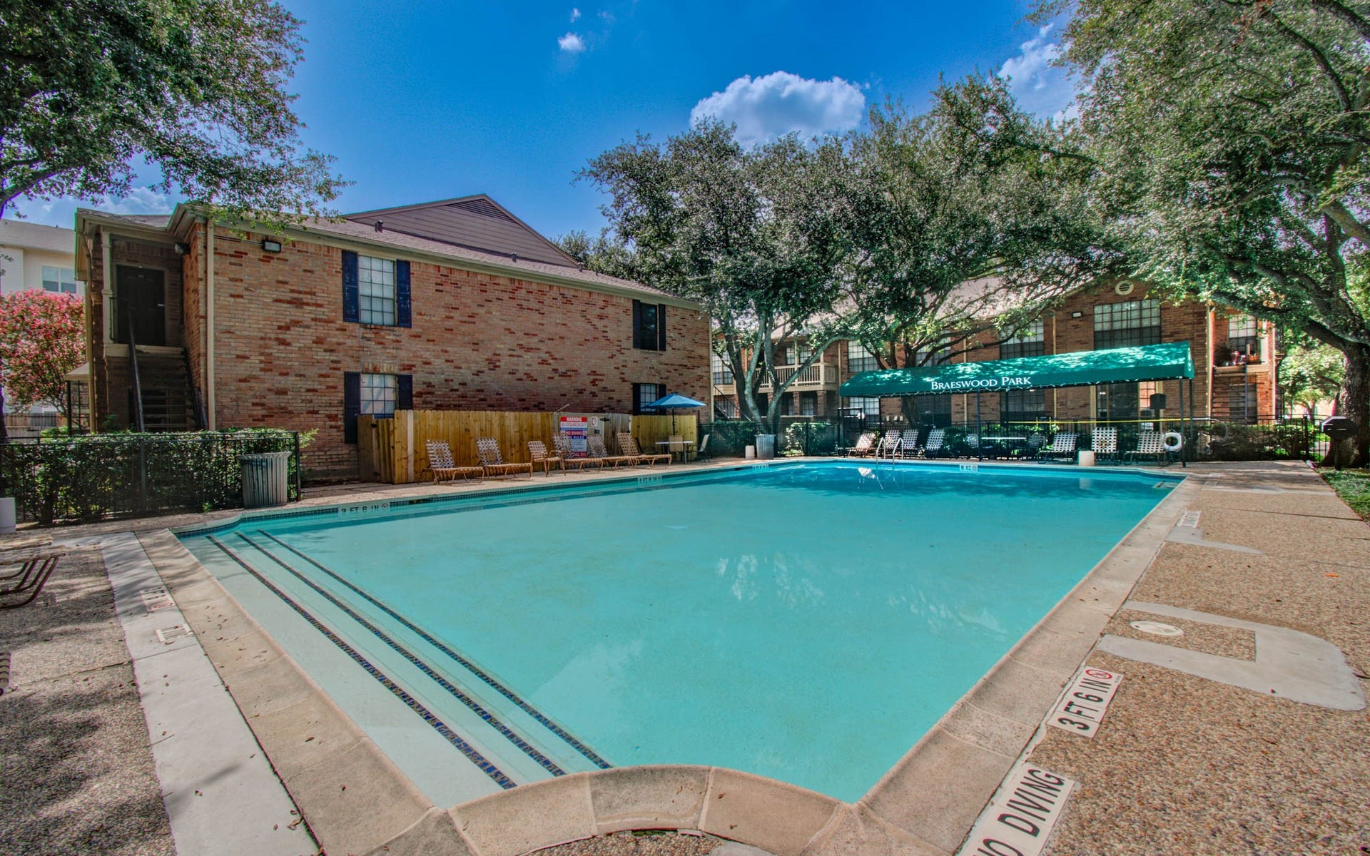 This photo showcases a community swimming pool surrounded by trees, featuring a shaded area with lounge chairs, perfect for relaxation and outdoor enjoyment.