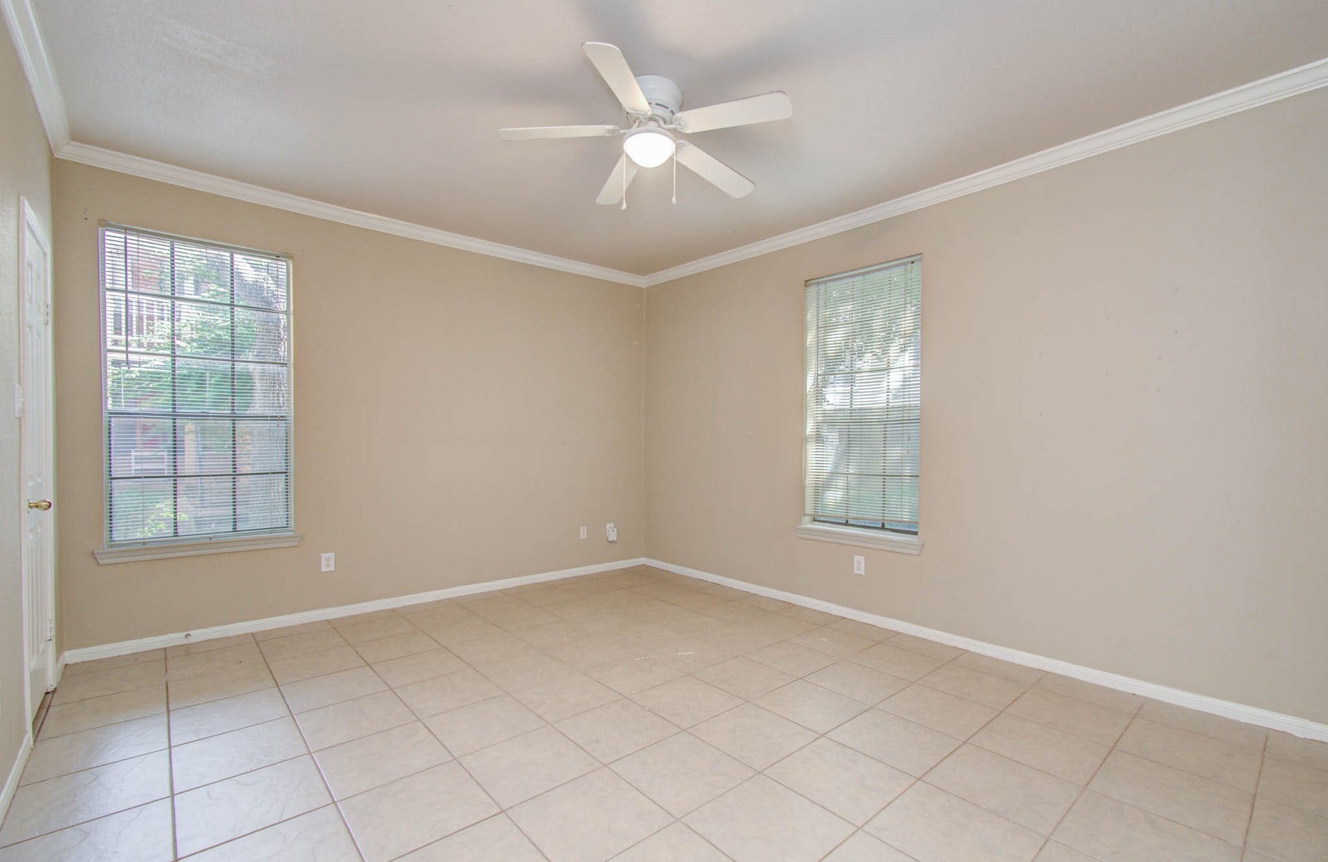 Bedroom features neutral walls, tile flooring, and ample natural light from two large windows.