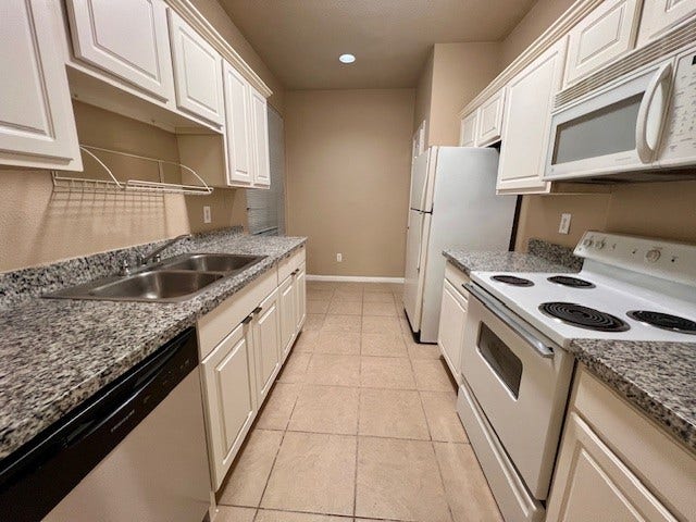 Kitchen features white cabinetry, granite countertops, and includes the refrigerator