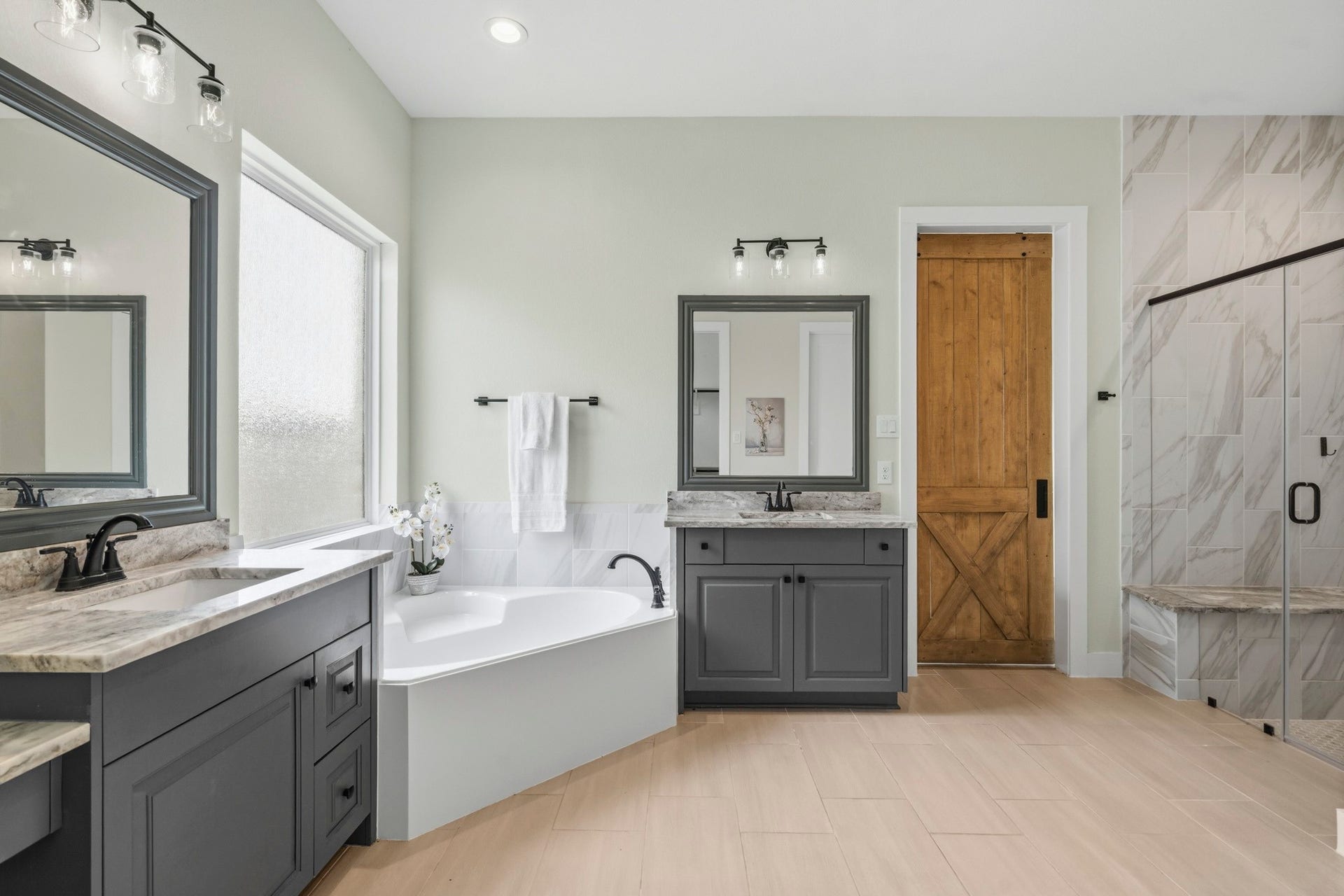 A corner garden tub serves as one focal point and is set beneath a large translucent window that fills the space with natural light while maintaining privacy. The oversized frameless, clear glass shower features a floor-to-ceiling marble-inspired tile and a lovely granite-topped bench seat. Completing this exceptional Bath are two oversized walk-in closets, providing abundant closet space.