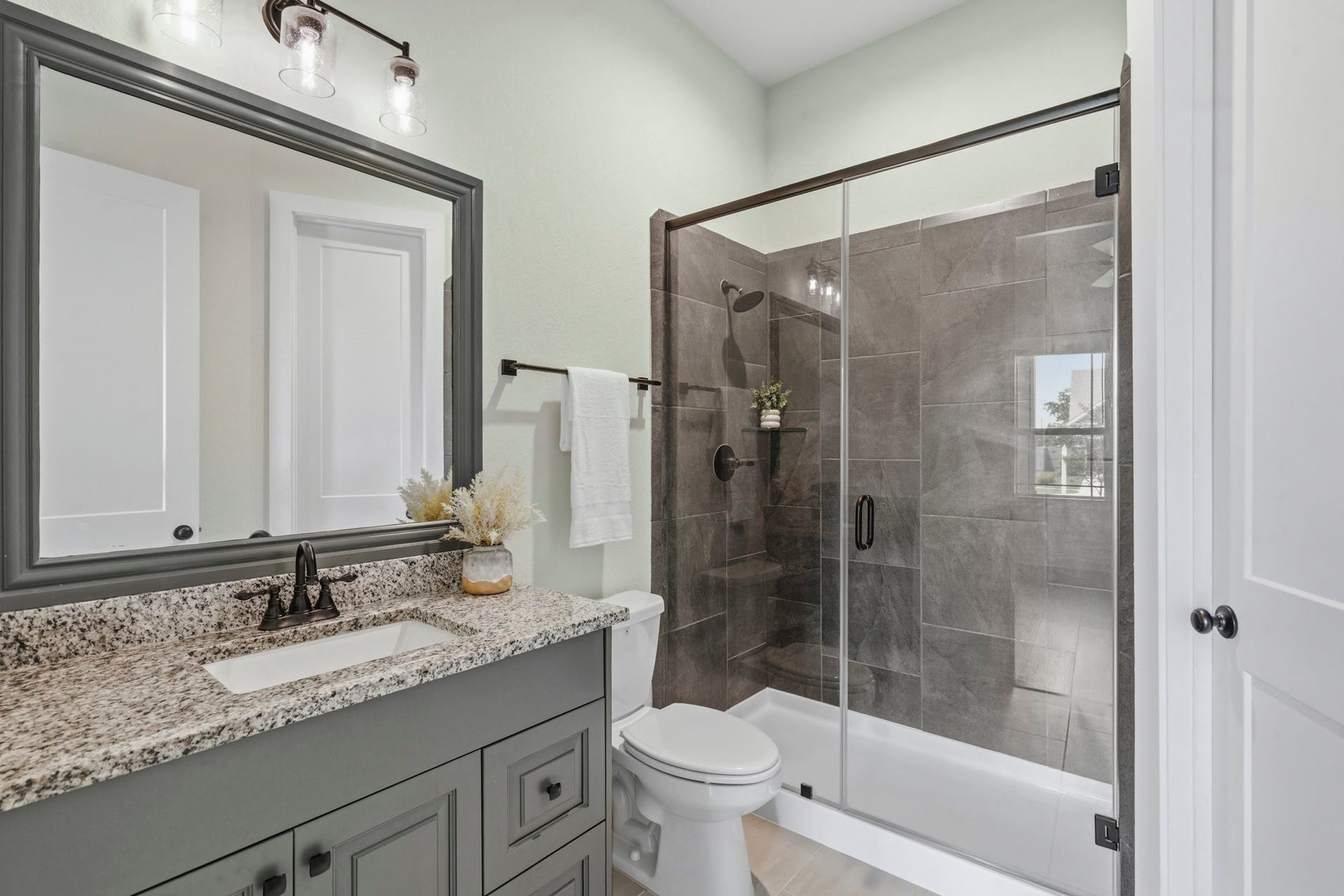 This Guest Bath combines timeless elegance with everyday functionality. The clear glass tub/shower serves as a striking focal point, finish in rich, dark tile that creates a more sophisticated ambiance and adds a sense of luxury to the room. It too, features an undermount sink, sleek granite countertops and a framed mirror.